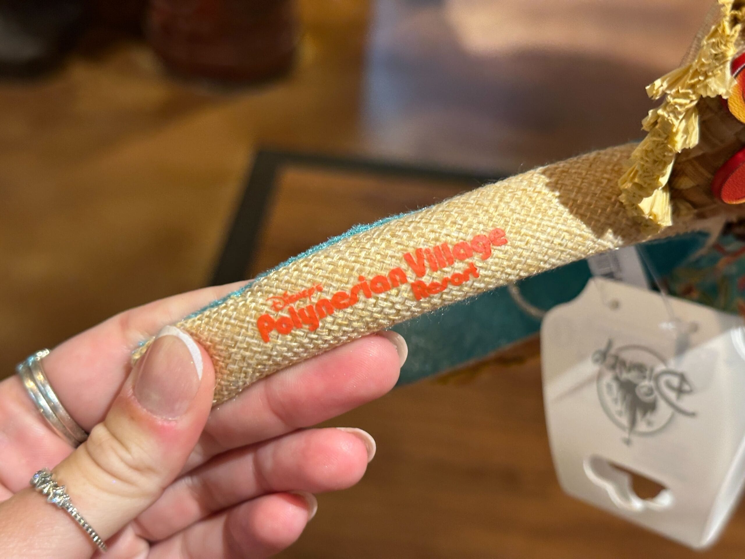 A hand holds a woven strap labeled "Disney Polynesian Village Resort" in red text.