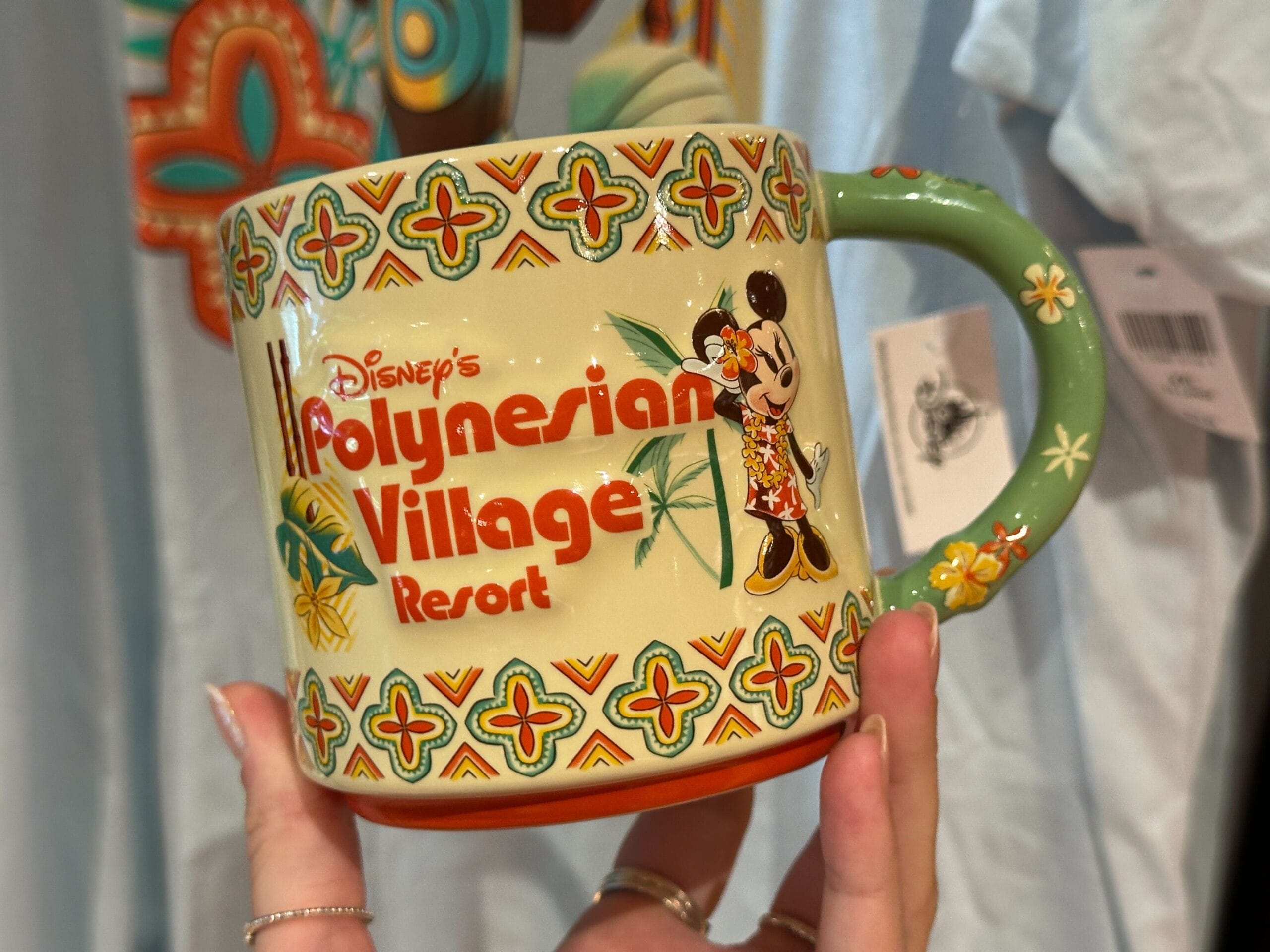 A hand holds a Disney's Polynesian Village Resort mug featuring Minnie Mouse in a tropical outfit and colorful patterns.