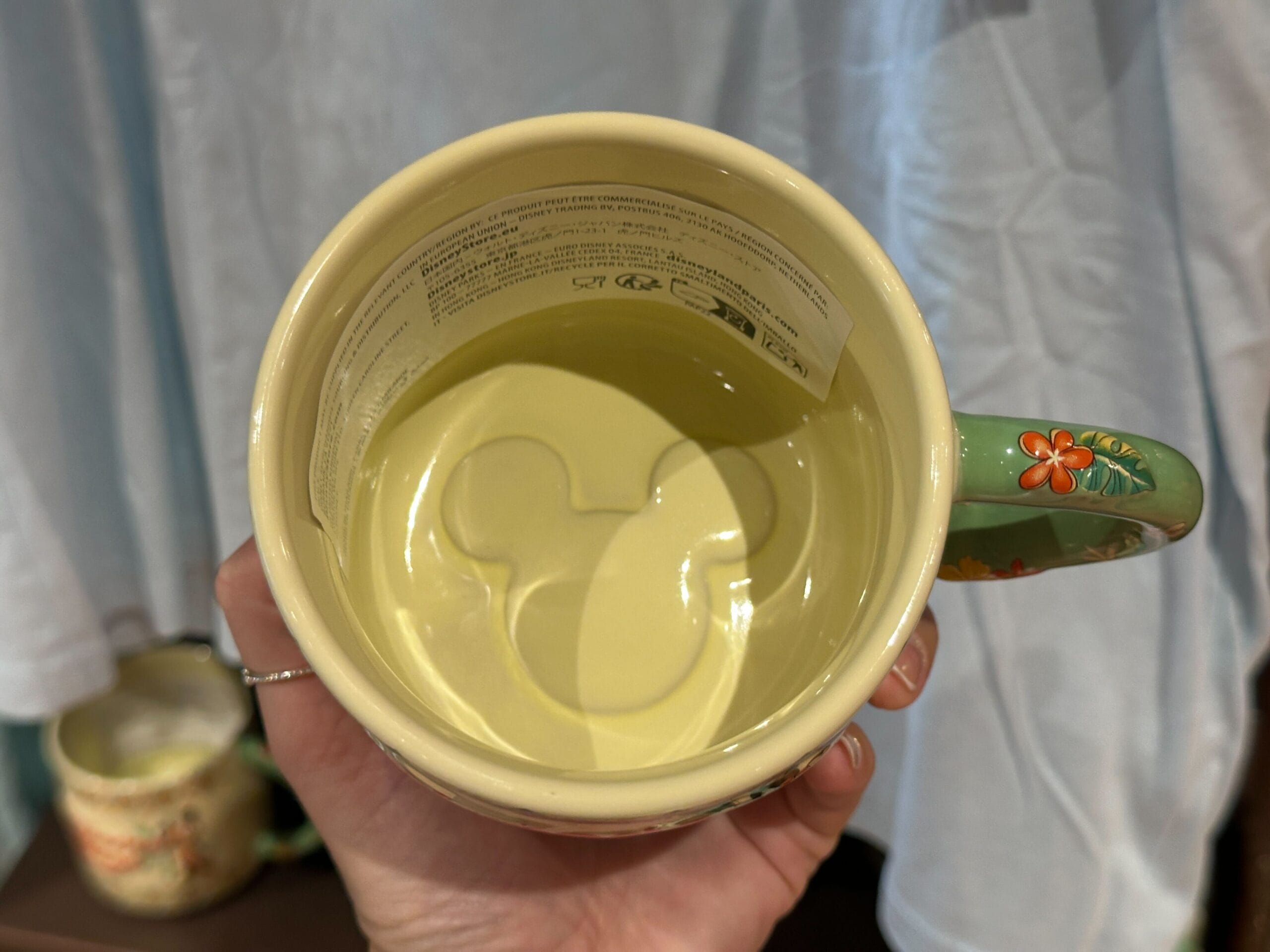 A hand holds a mug with a Mickey Mouse head shape embossed inside the bottom.