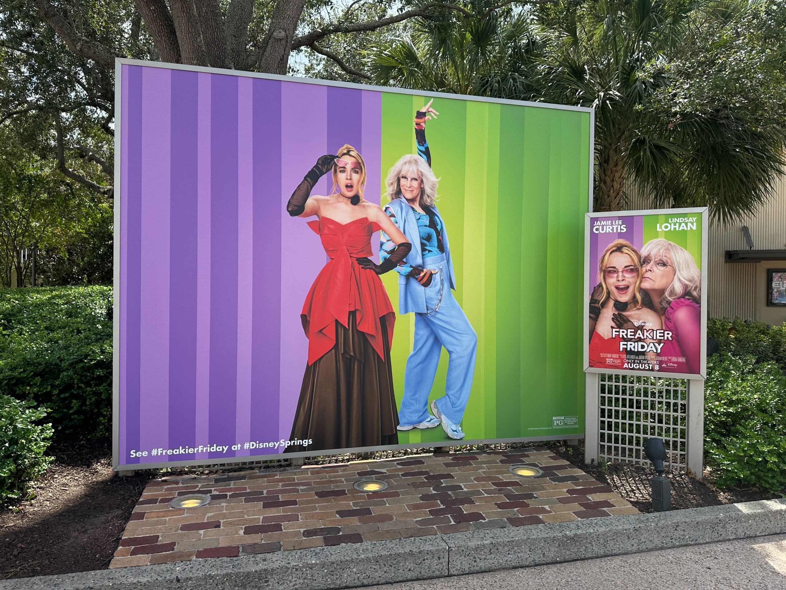 Large outdoor sign shows two women in swapped costumes, promoting "Freaky Friday" next to a smaller movie poster.