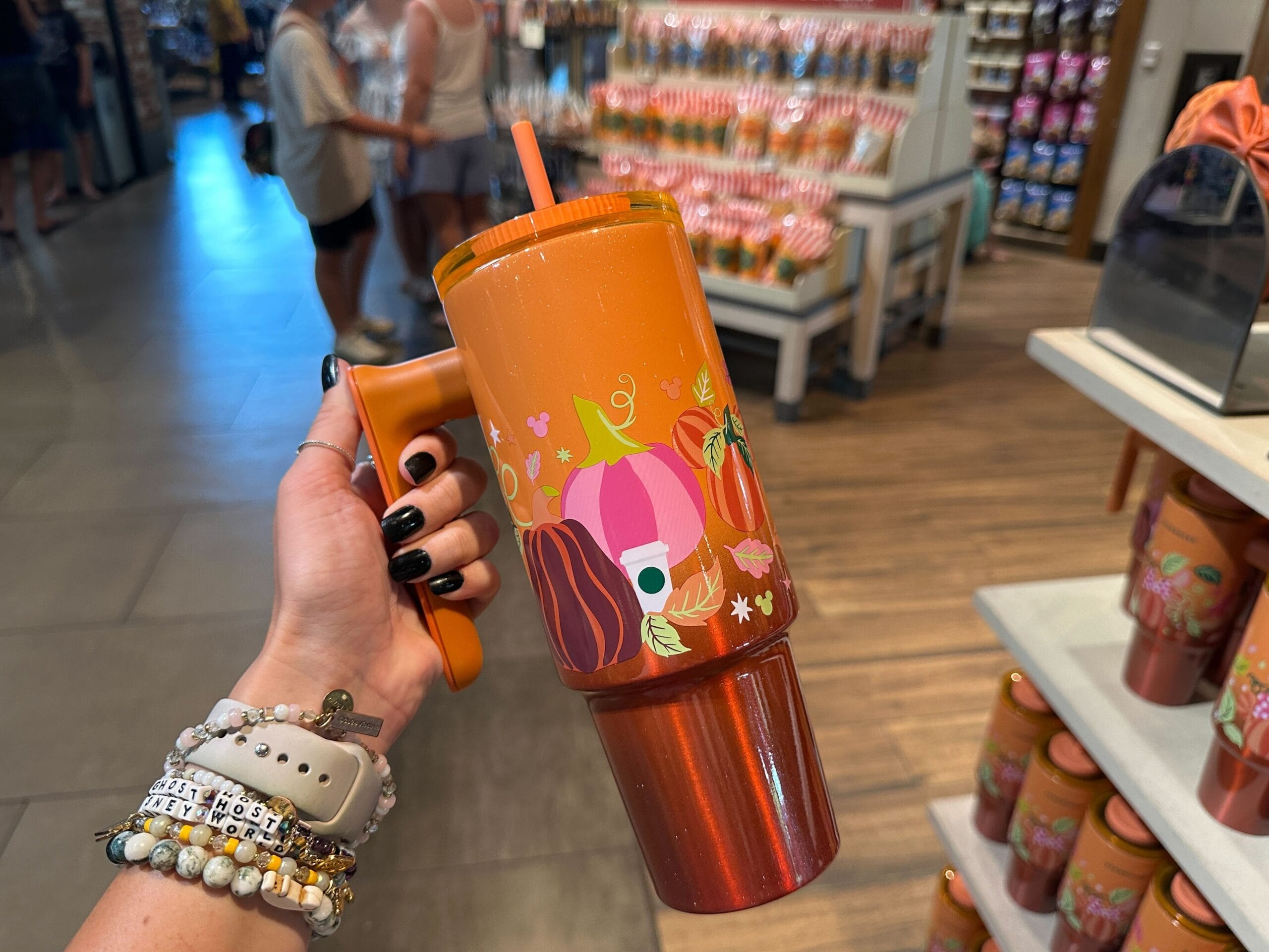 Hand holding an orange tumbler with pumpkin and floral designs from Starbucks Pumpkin Spice merchandise collection in store.
