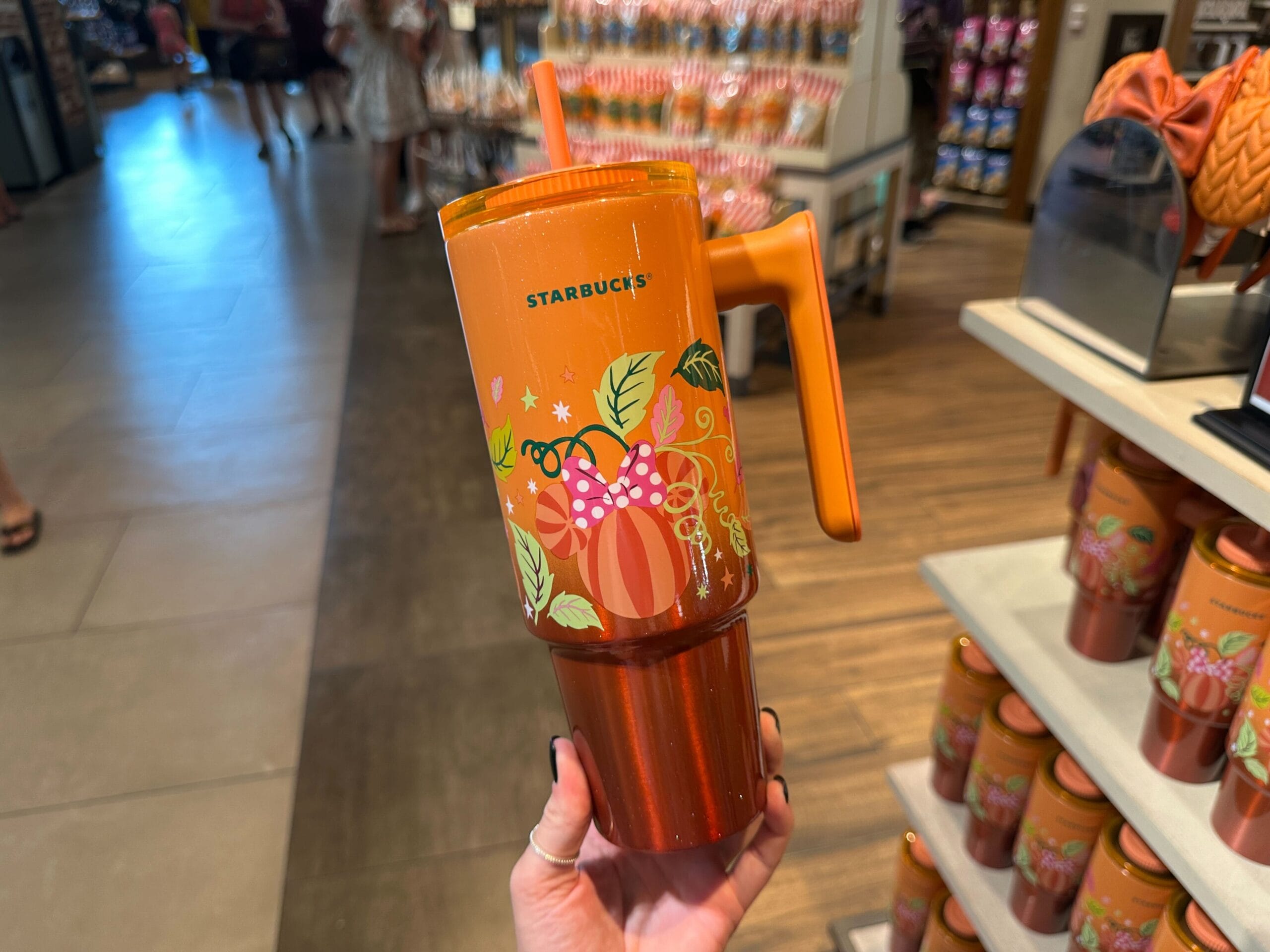 Hand holding an orange Starbucks tumbler with pumpkin and leaf designs, perfect for Pumpkin Spice Merchandise fans.