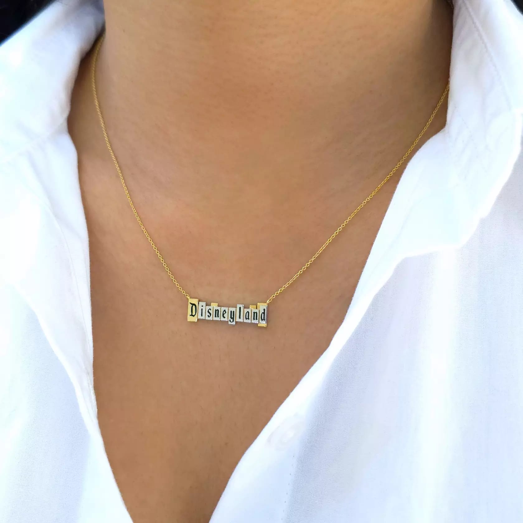 Close-up of a woman's neck modeling a necklace from the CRISLU Disneyland Marquee Collection with a Disneyland marquee pendant in platinum on a gold chain.