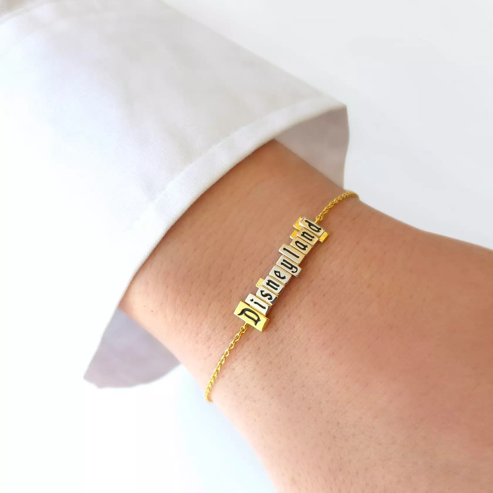 Wrist with a chain bracelet from the CRISLU Disneyland Marquee Collection with a Disneyland marquee pendant in platinum on a gold chain.