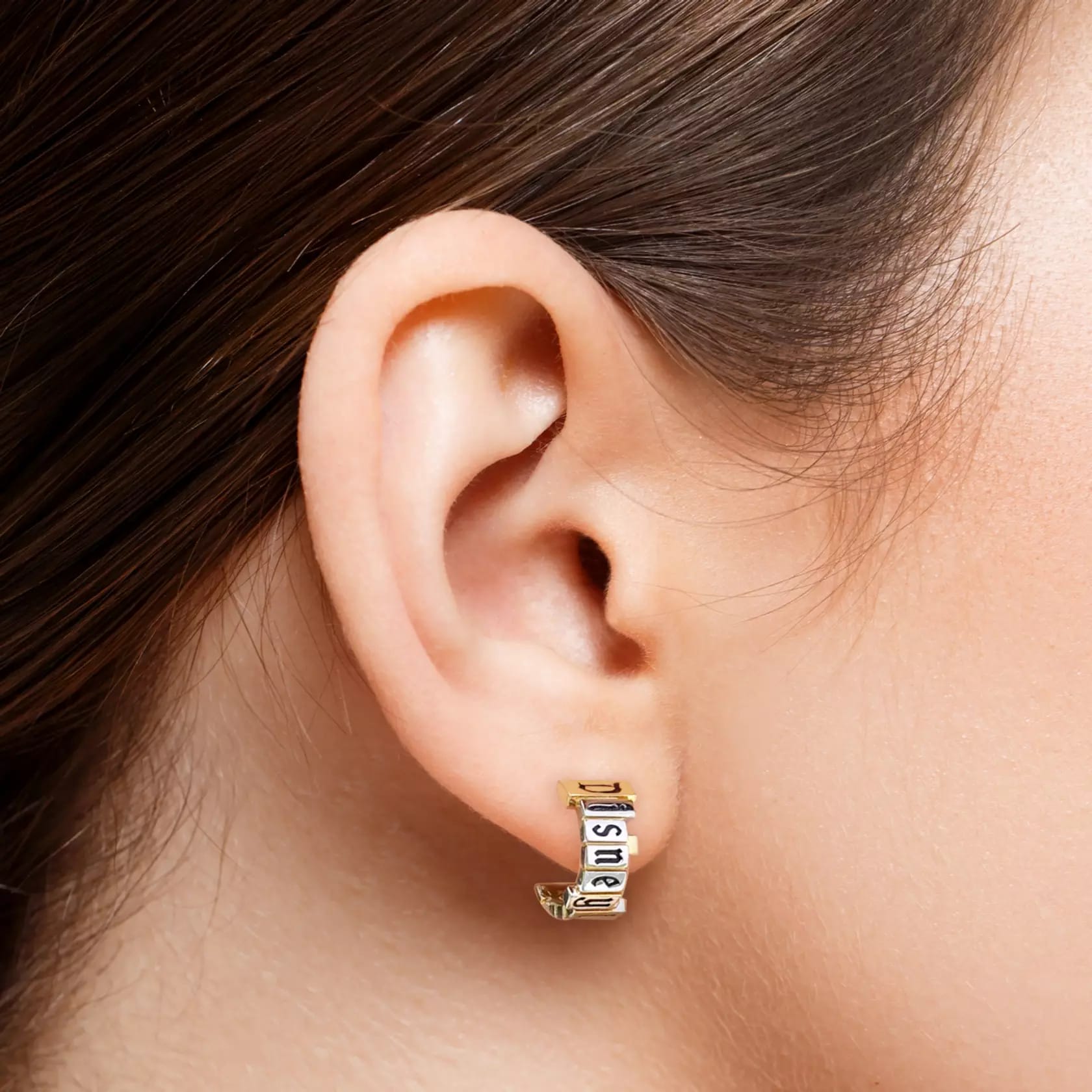 Close-up of an ear wearing a hoop earring from the CRISLU Disneyland Marquee Collection with the Disneyland marquee in platinum on a gold base.