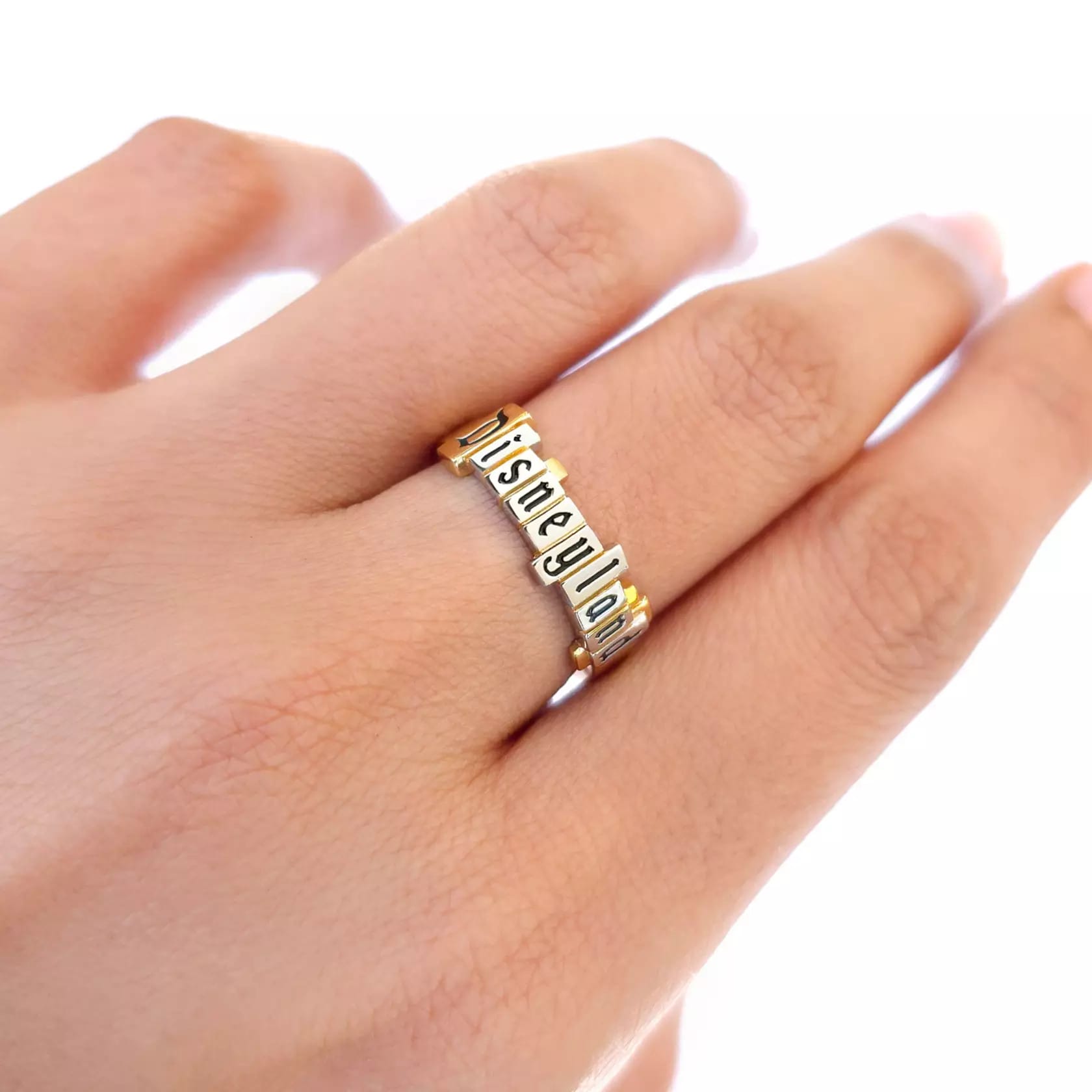 Hand wearing a gold ring from the CRISLU Disneyland Marquee Collection with the Disneyland marquee in platinum on a gold ring with a single cubic zirconia.