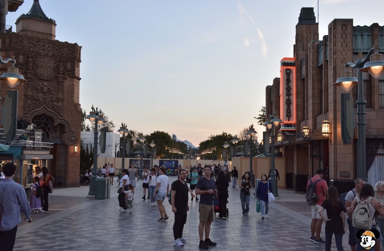 People walk through an outdoor plaza at sunset, surrounded by ornate buildings and streetlights.