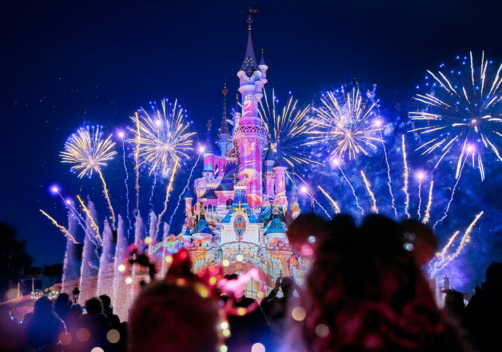 Colorful fireworks light up the night sky behind Disneyland Paris’s fairytale castle, with crowds watching in silhouette.