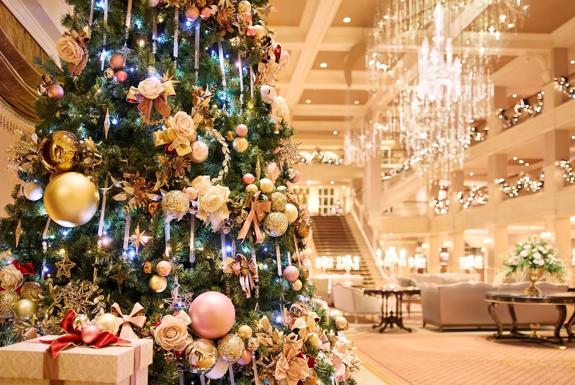 Elegant Christmas tree with gold ornaments and lights in a luxurious hotel lobby at Disneyland Paris, presents below.