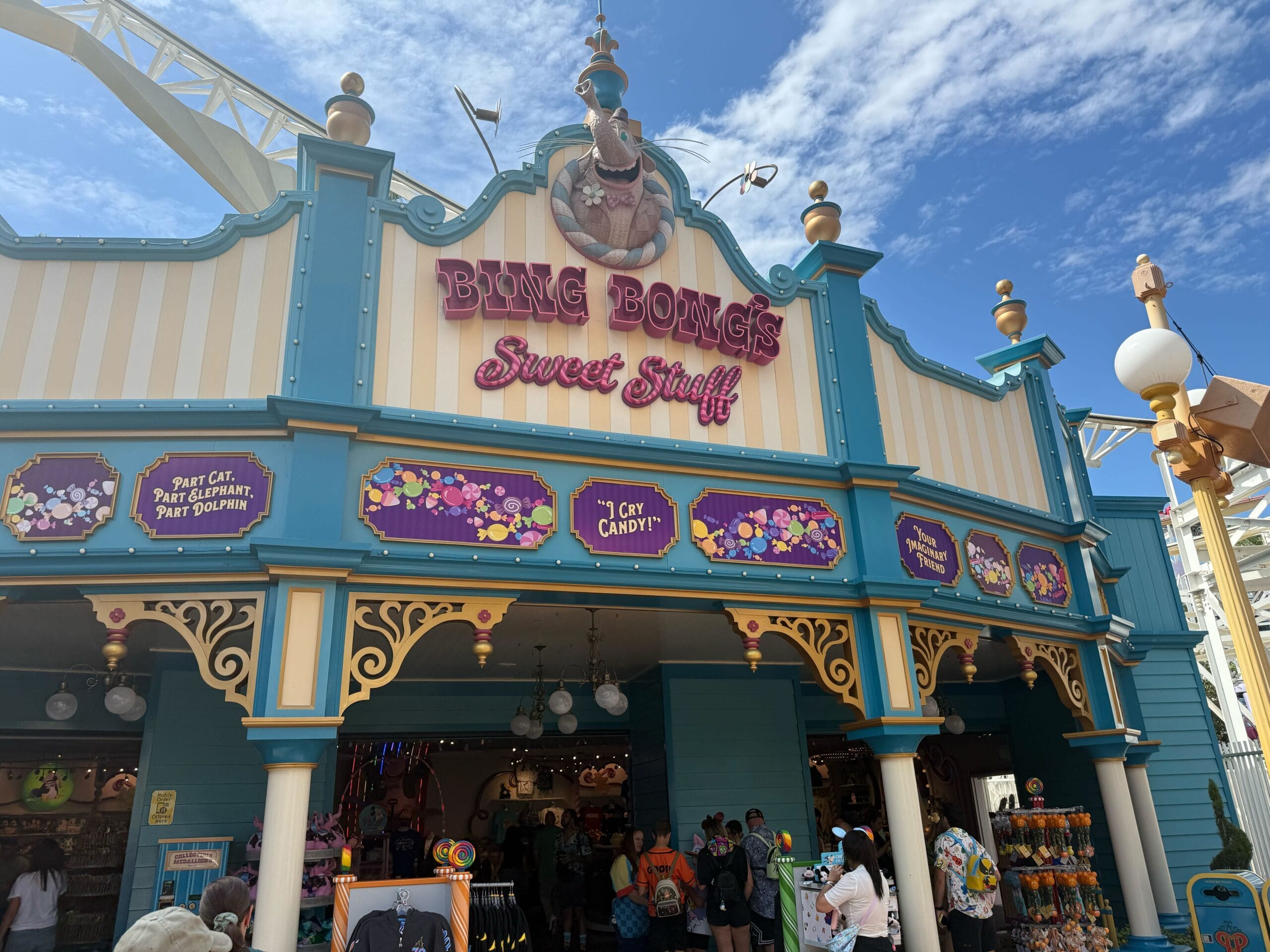 Colorful candy shop exterior at Disneyland with the "Bing Bong’s Sweet Stuff" sign, people entering under a blue sky.