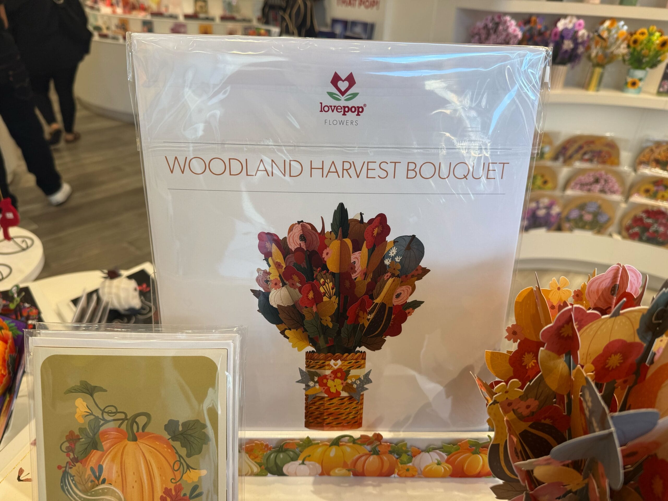 A display of a Lovepop "Woodland Harvest Bouquet" card featuring a colorful paper bouquet and autumn-themed designs.