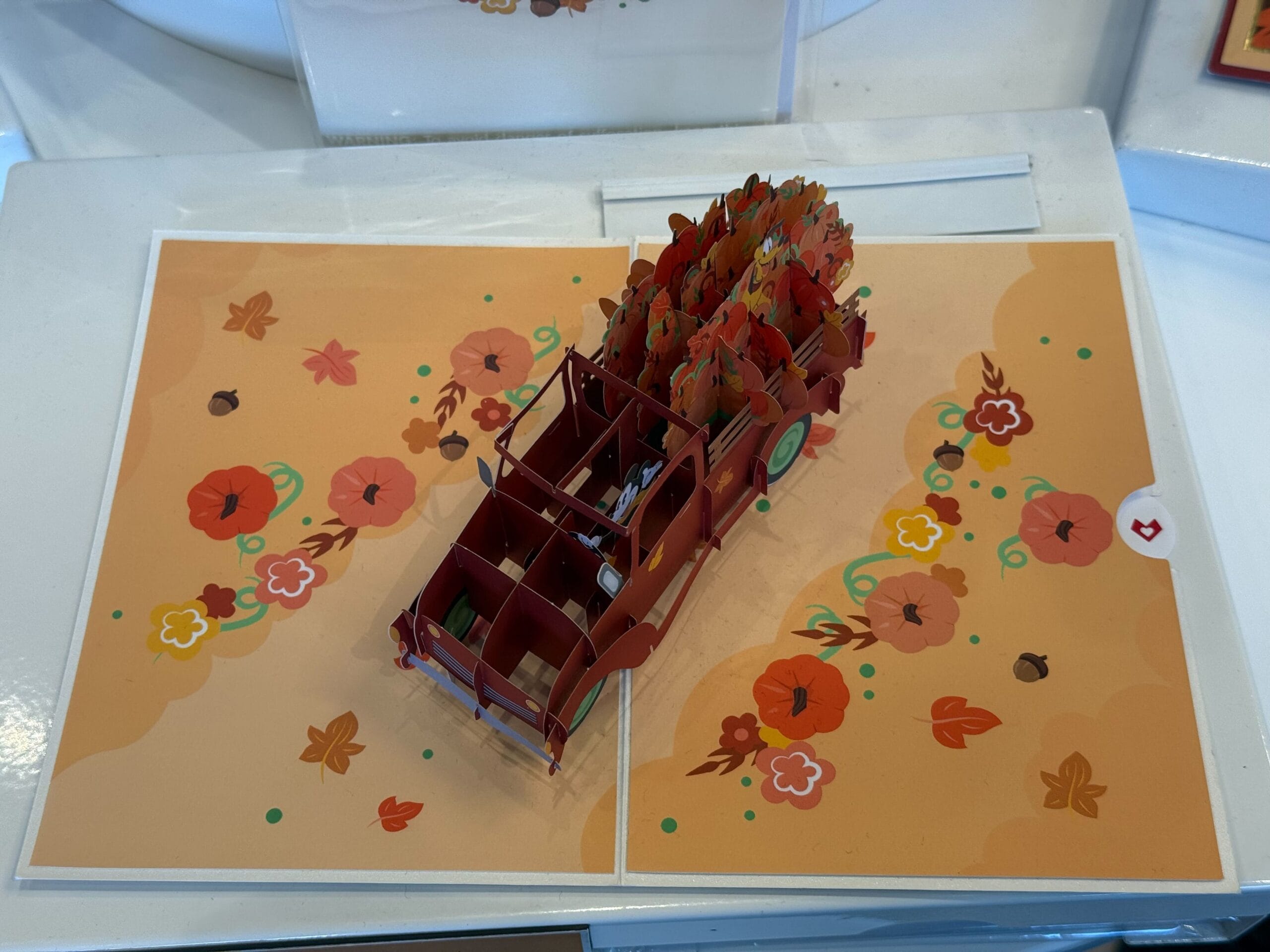 A pop-up card features a 3D red truck filled with autumn leaves and flowers on an orange floral background.