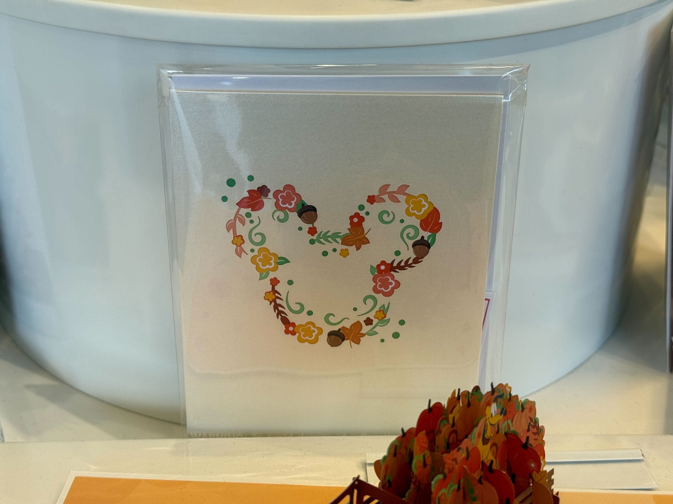 A card with a floral design shaped like Mickey Mouse’s head, displayed upright in clear packaging.
