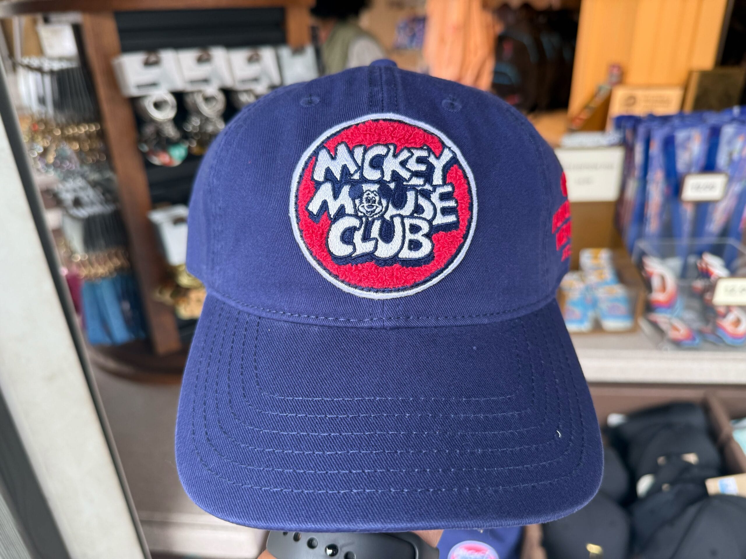 A navy blue cap with a red and white "Mickey Mouse Club" patch, perfect for Disneyland’s 70th Anniversary.