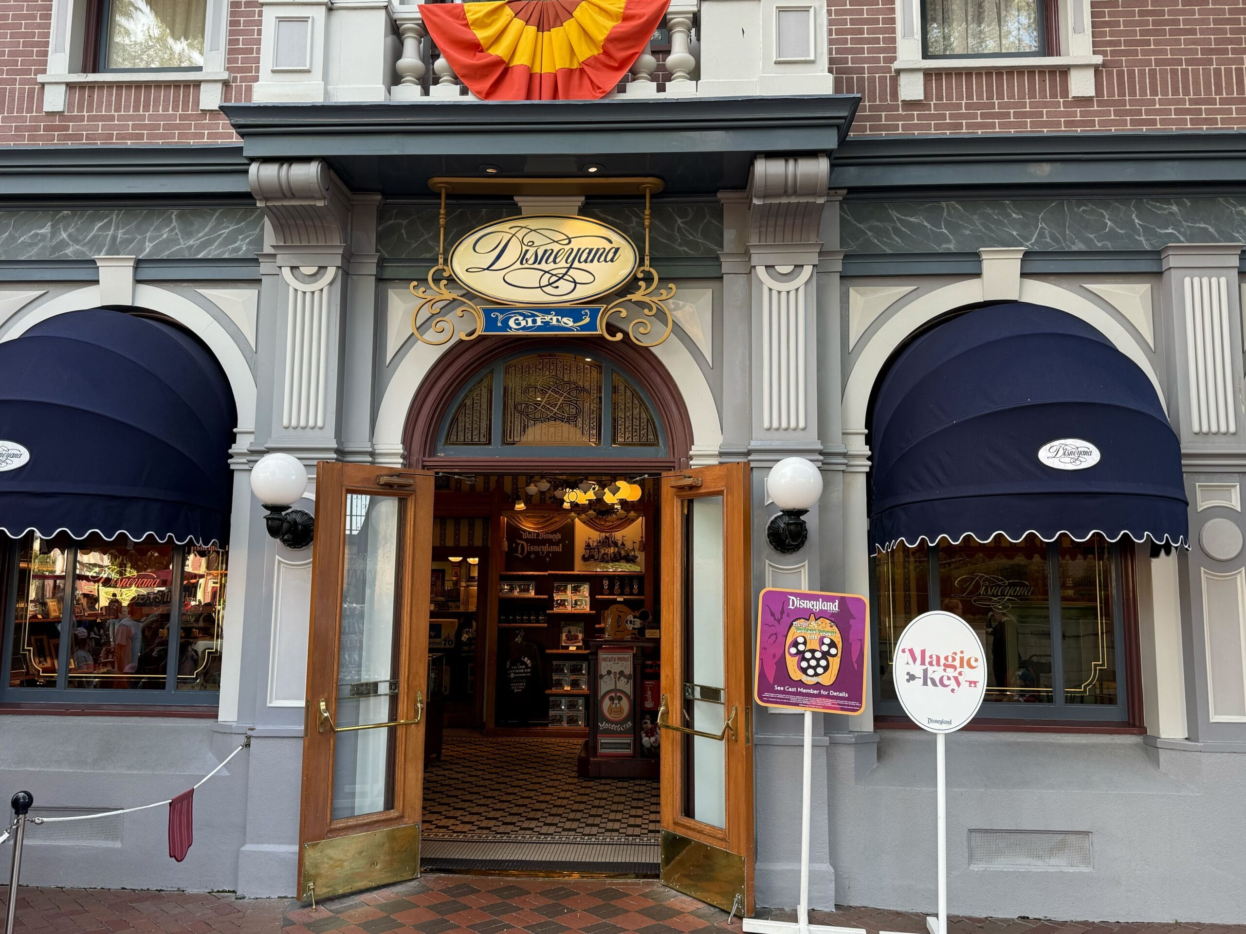 Entrance to the Disneyland Emporium with open doors, colorful signs, and 70th Anniversary Mickey Mouse Club merchandise.
