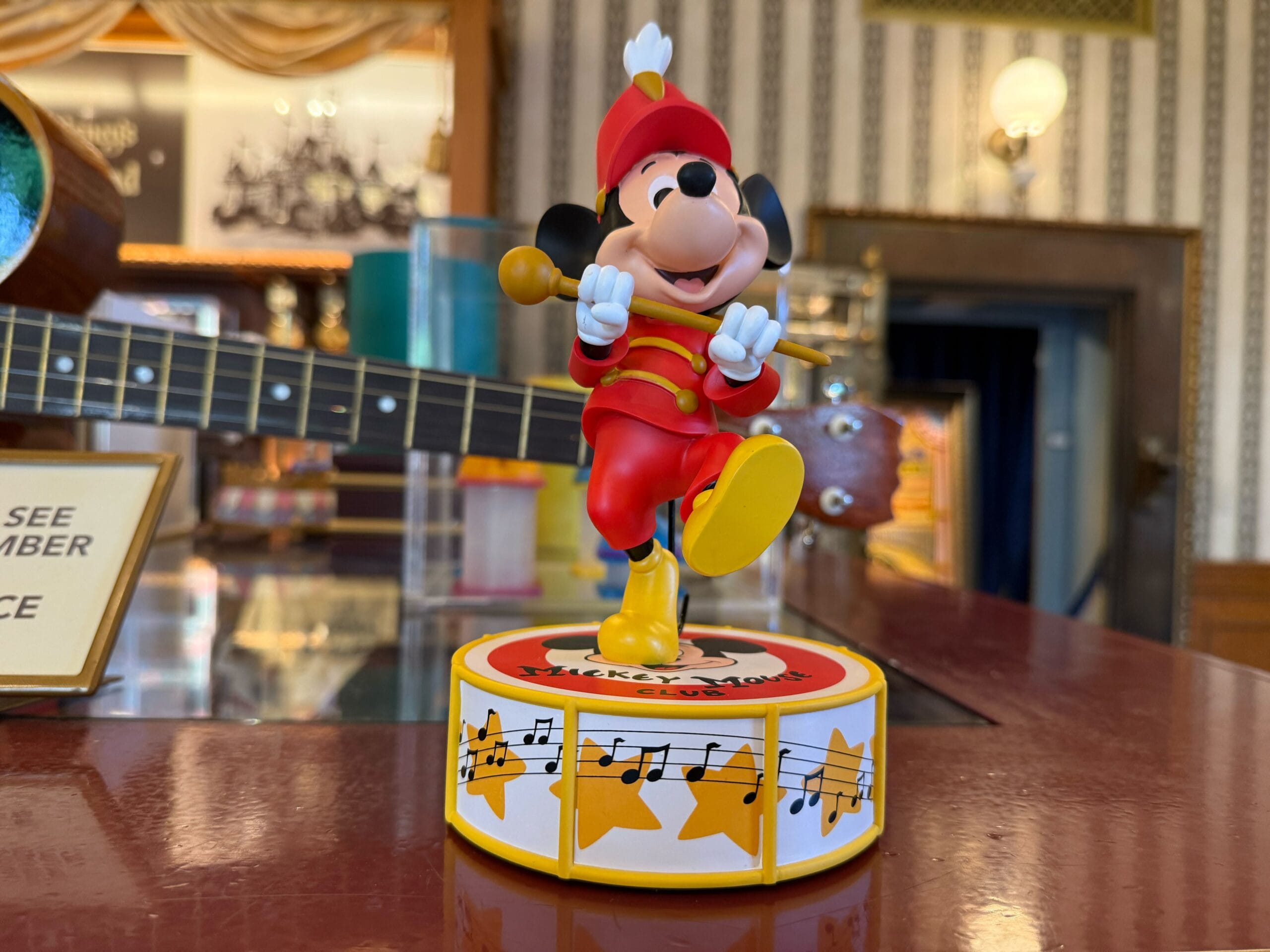 A Mickey Mouse Club merchandise figurine dressed as a band leader stands on a starry, musical drum.