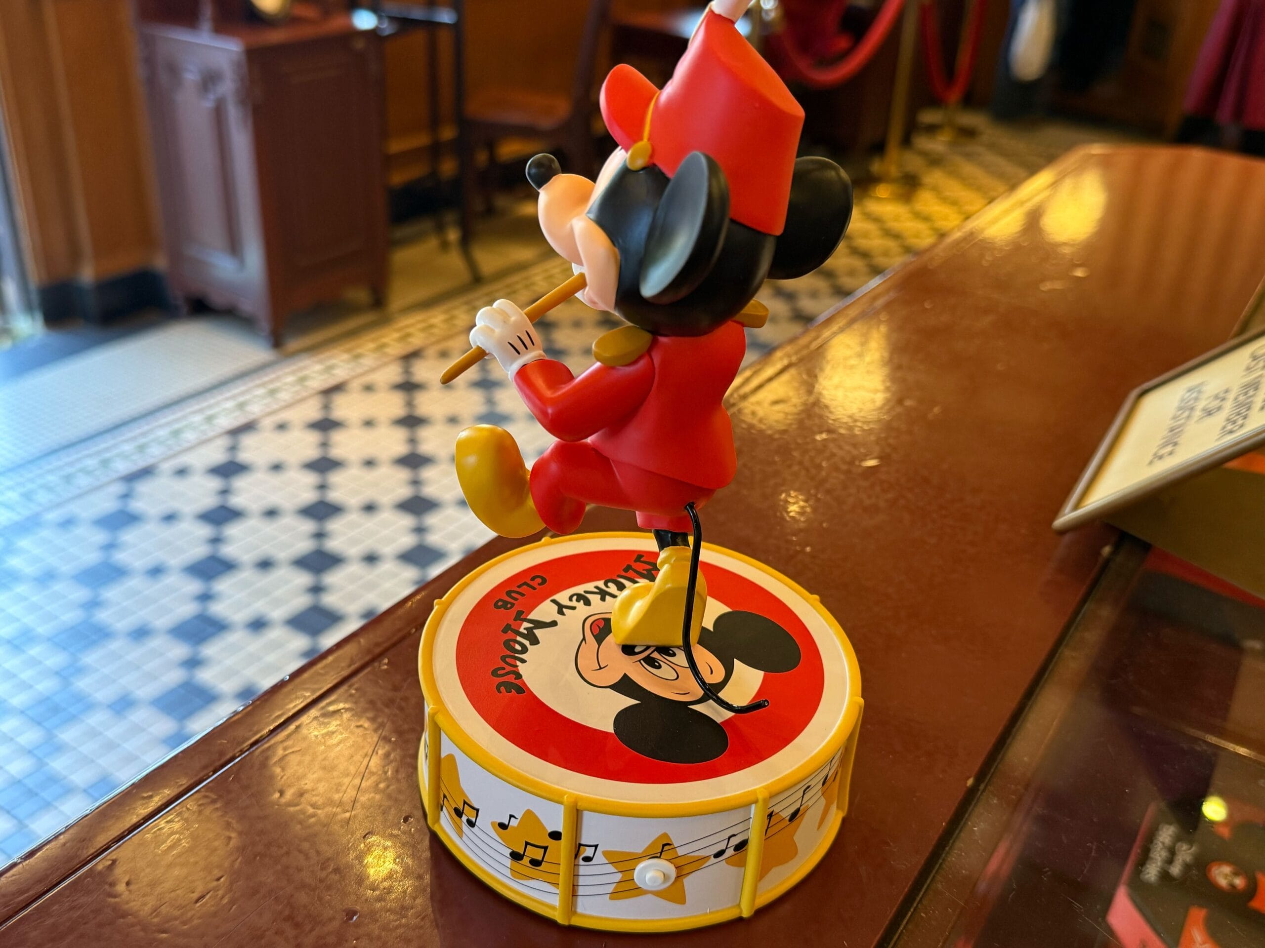 A Disneyland merchandise figurine of Mickey Mouse in a red band uniform stands on a 70th Anniversary Mickey Mouse Club drum.