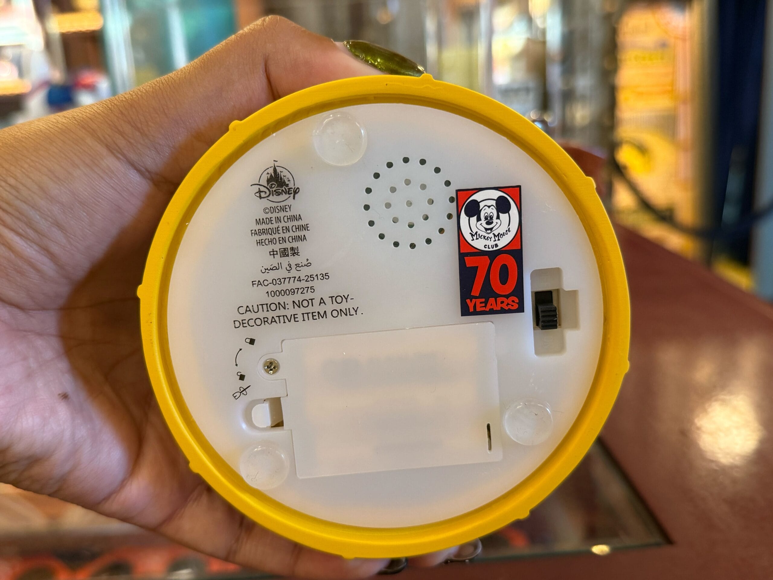 Hand holding a yellow Disneyland item’s base with a 70th anniversary Mickey Mouse Club merchandise sticker visible.