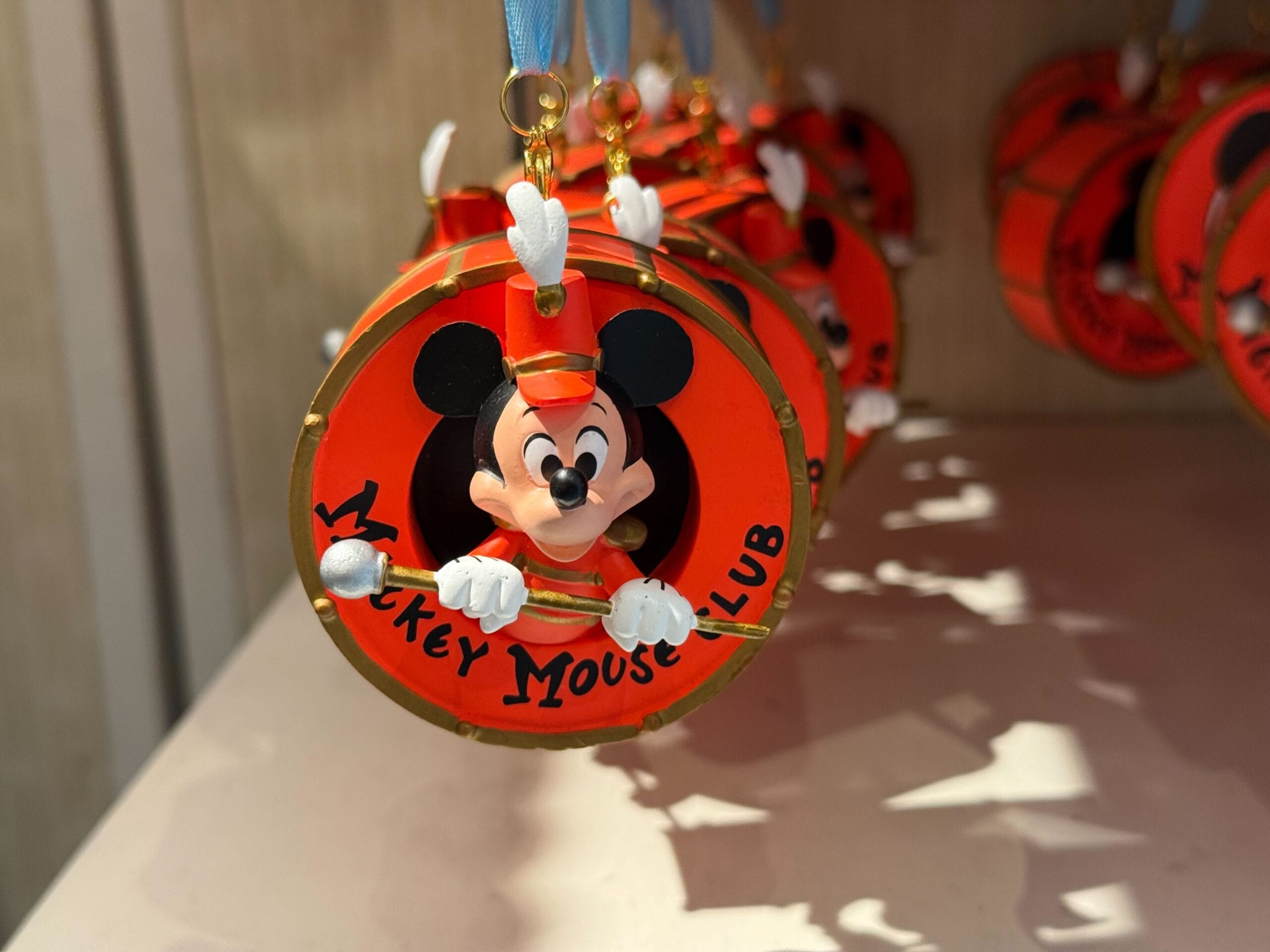 A round red Mickey Mouse Club ornament, 70th anniversary merchandise, shows Mickey with drumsticks on display.