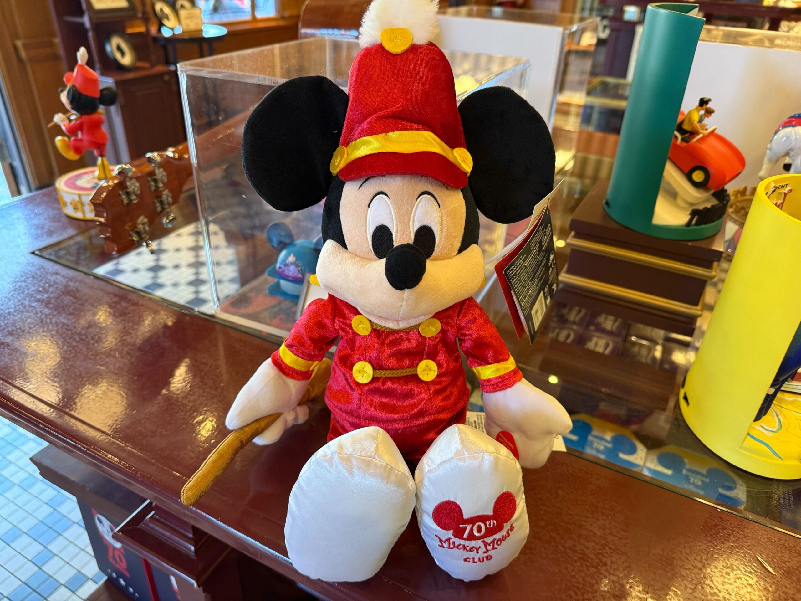 Plush Mickey Mouse in a red band uniform with "70th anniversary" on his shoe—a must-have Mickey Mouse Club merchandise.