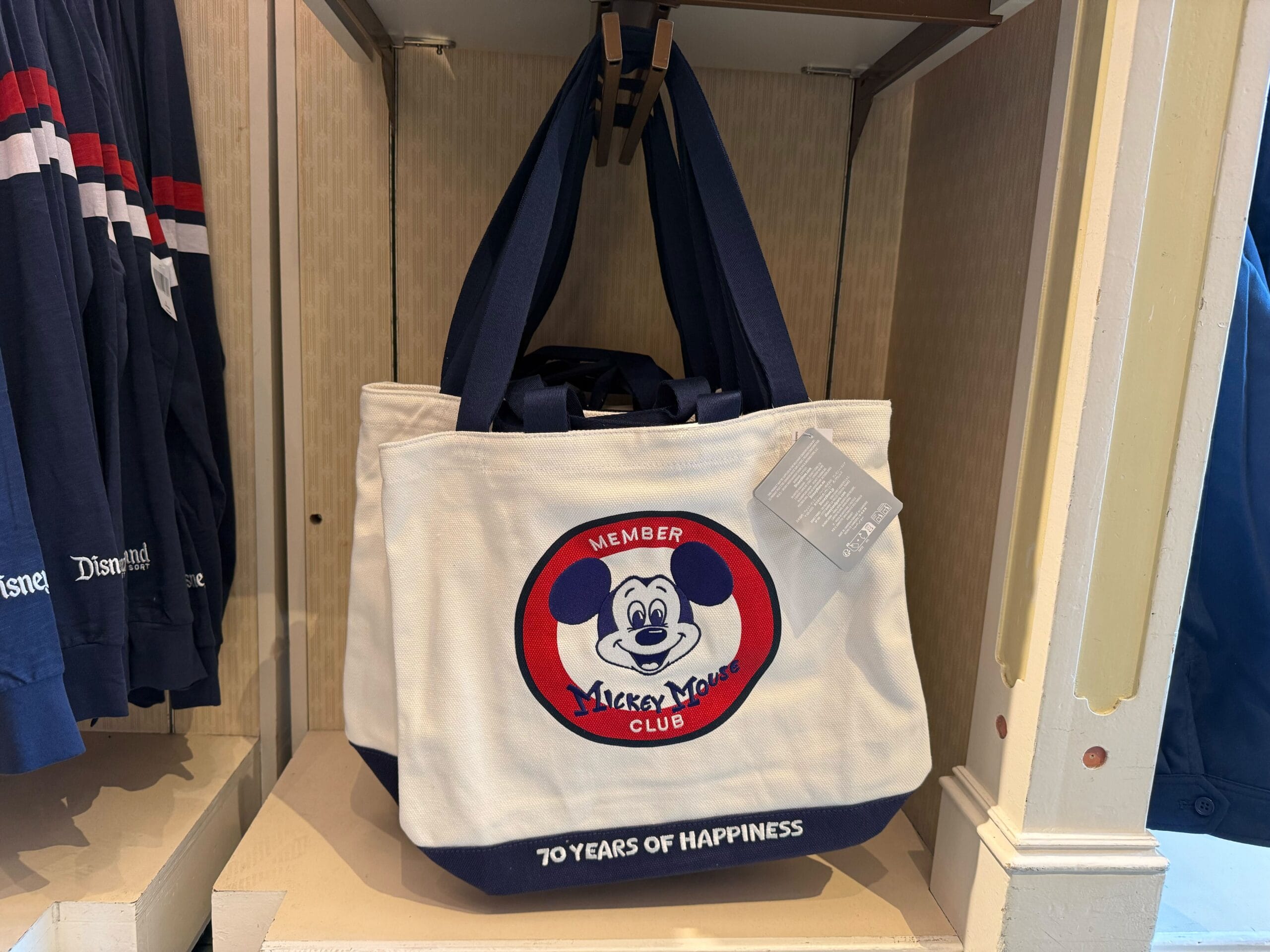 White tote bag featuring Mickey Mouse Club merchandise and "70 Years of Happiness" on display at Disneyland.
