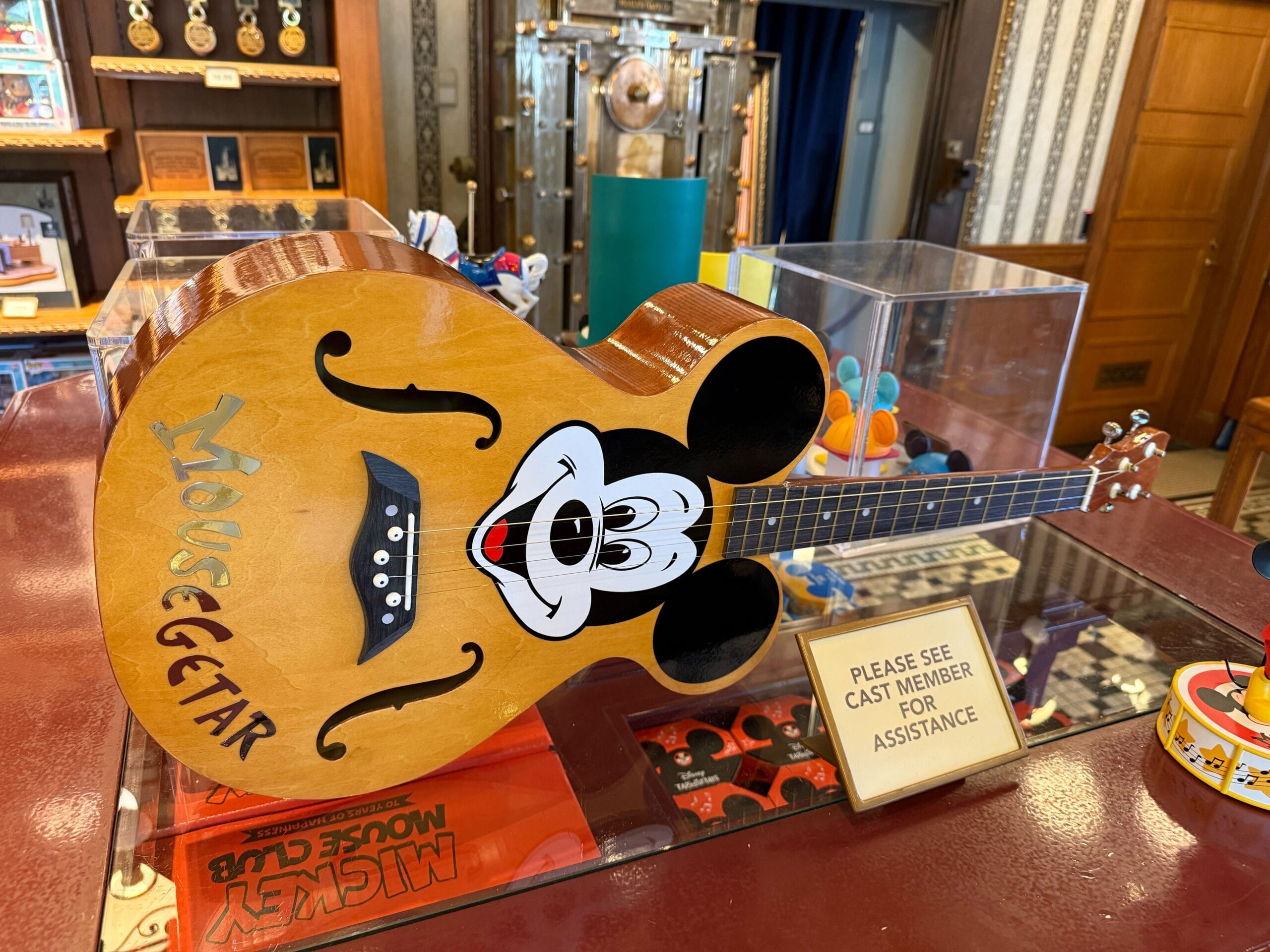 An acoustic guitar labeled "Mousegetar" with a Mickey face, part of Mickey Mouse Club merchandise at Disneyland.