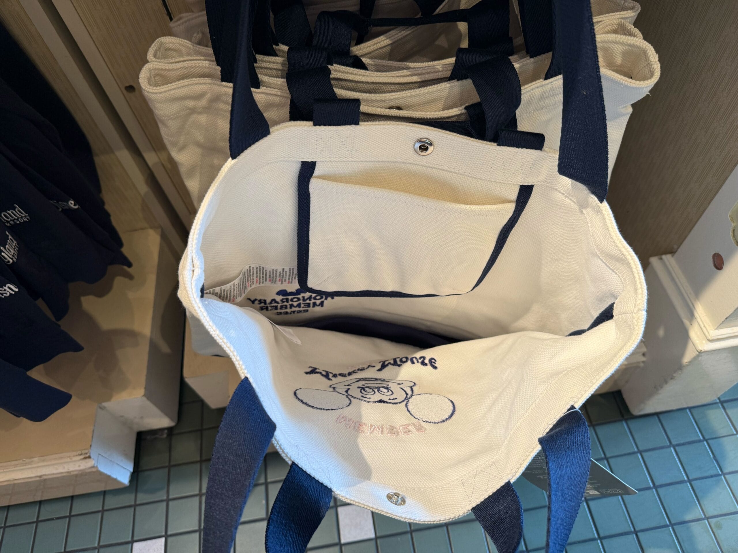 Open white canvas tote bag with navy straps, inner pocket, and Mickey Mouse Club cartoon embroidery on the lining.