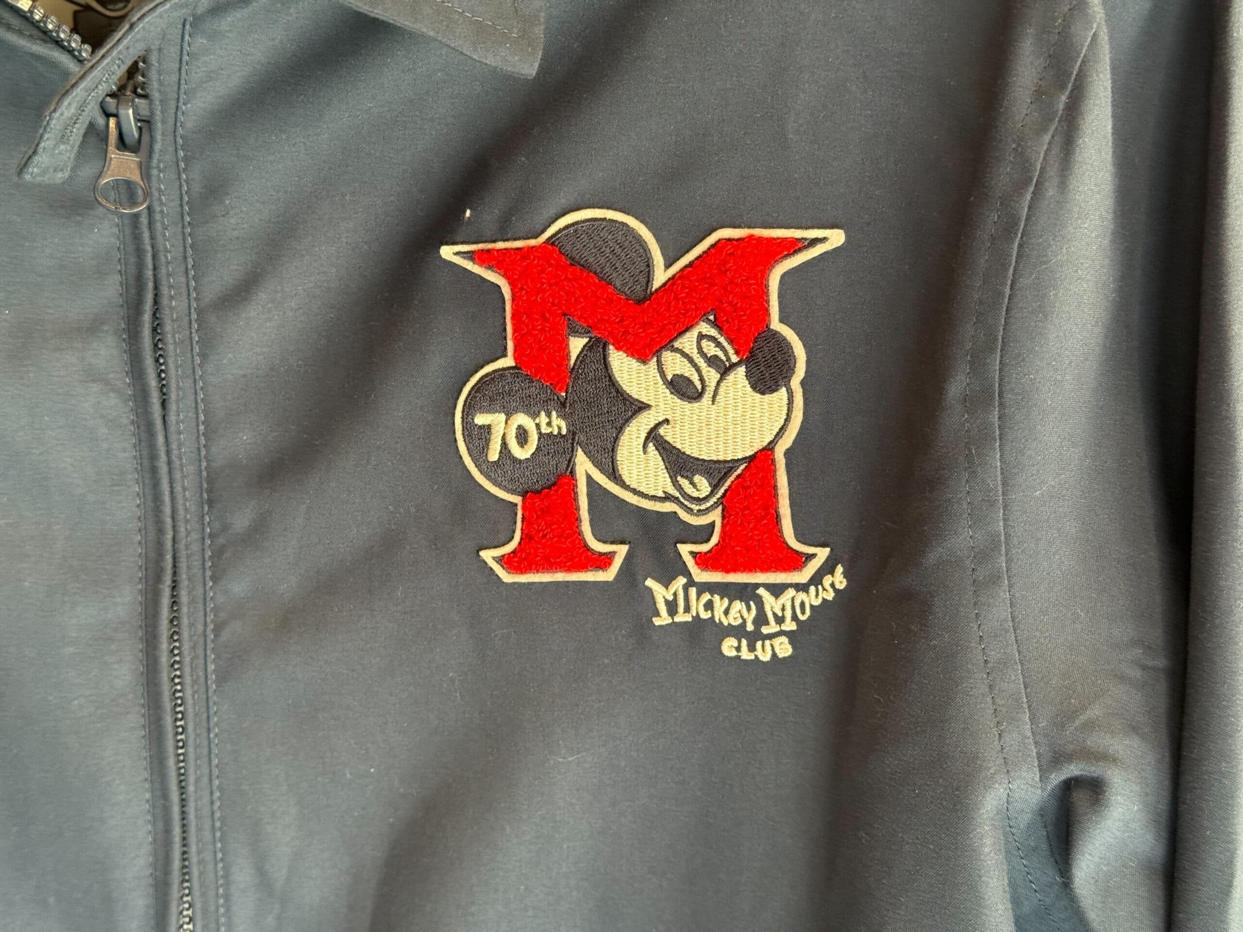 Black jacket with a red "M," Mickey Mouse face, and 70th anniversary Mickey Mouse Club merchandise patch.
