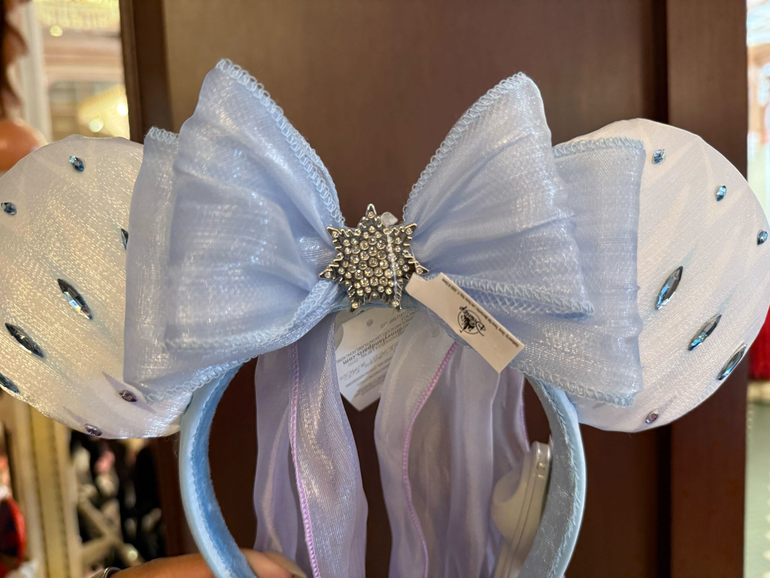 Light blue Minnie Mouse Elsa Ear Headband with a large bow and silver snowflake brooch, perfect for Disneyland.
