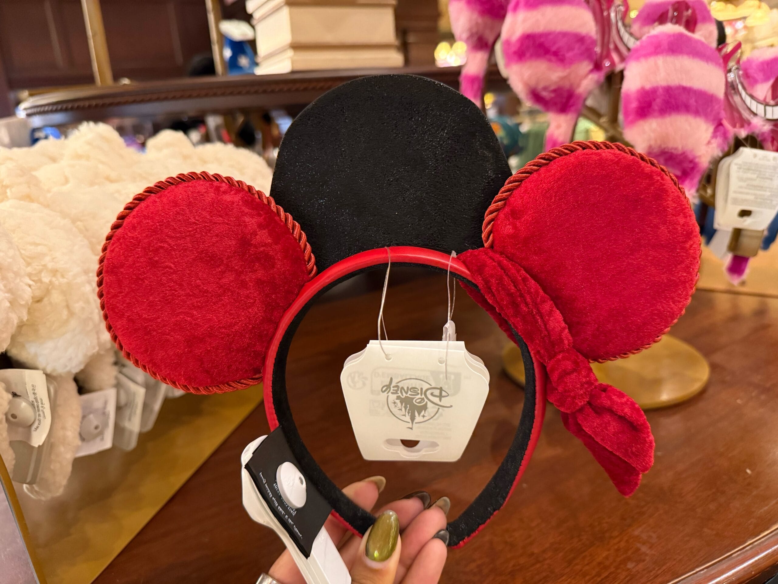 Red and black Minnie Mouse ear headband with a bow, spotted at Disneyland among plush toys in the background.