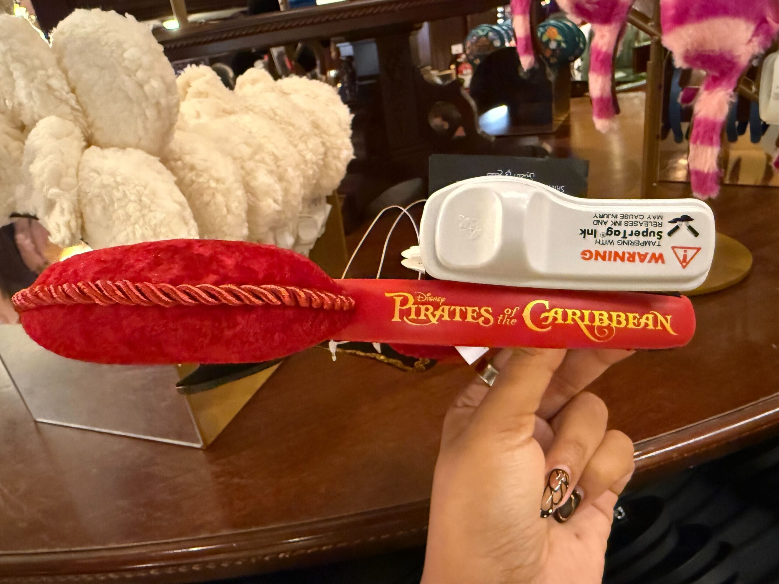 Hand holding a red plush sword with "Pirates of the Caribbean" text, on display at Disneyland.