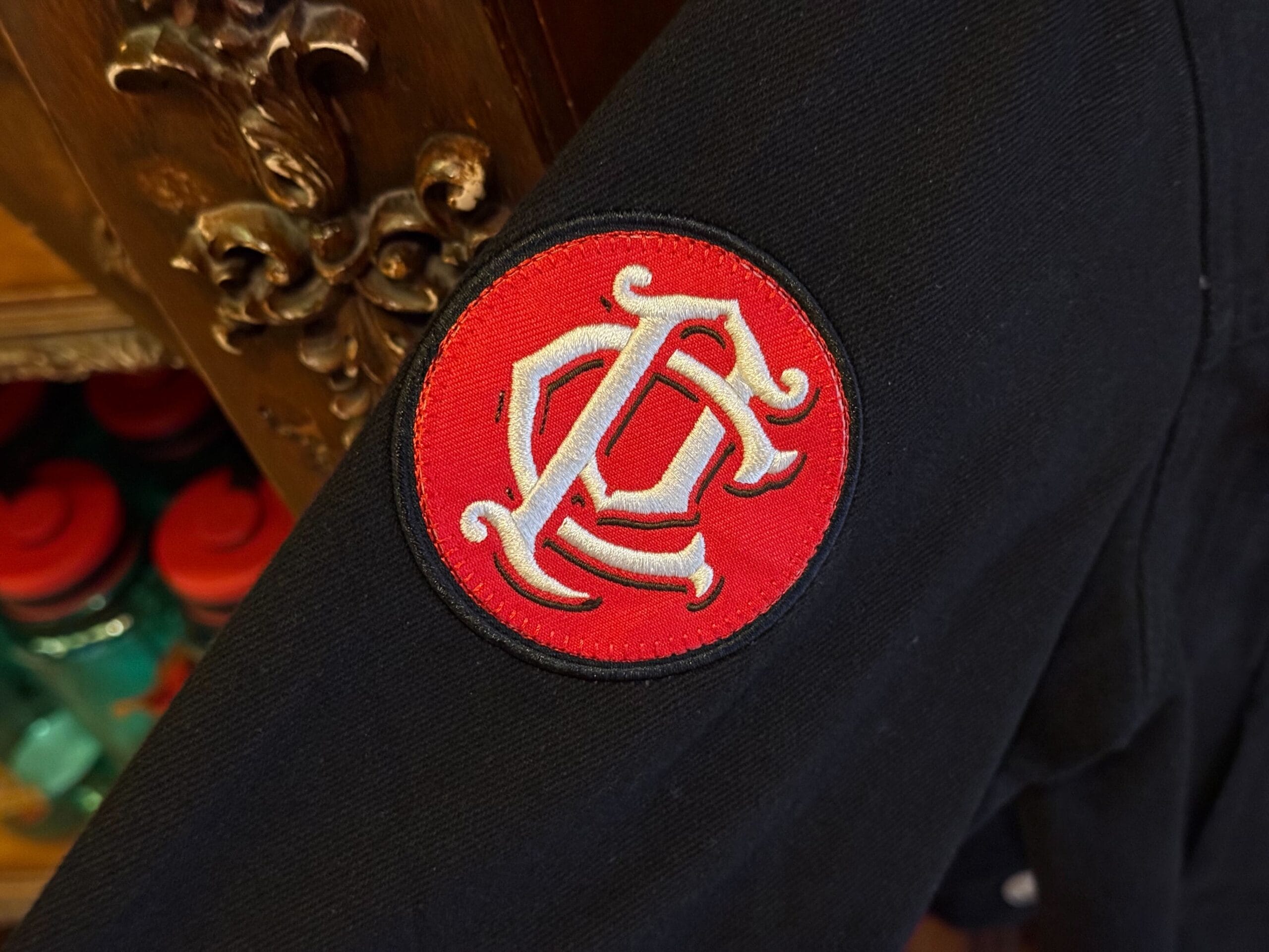 A red and white embroidered patch with ornate "C" and "L" adorns black apparel, inspired by Pirates of the Caribbean.
