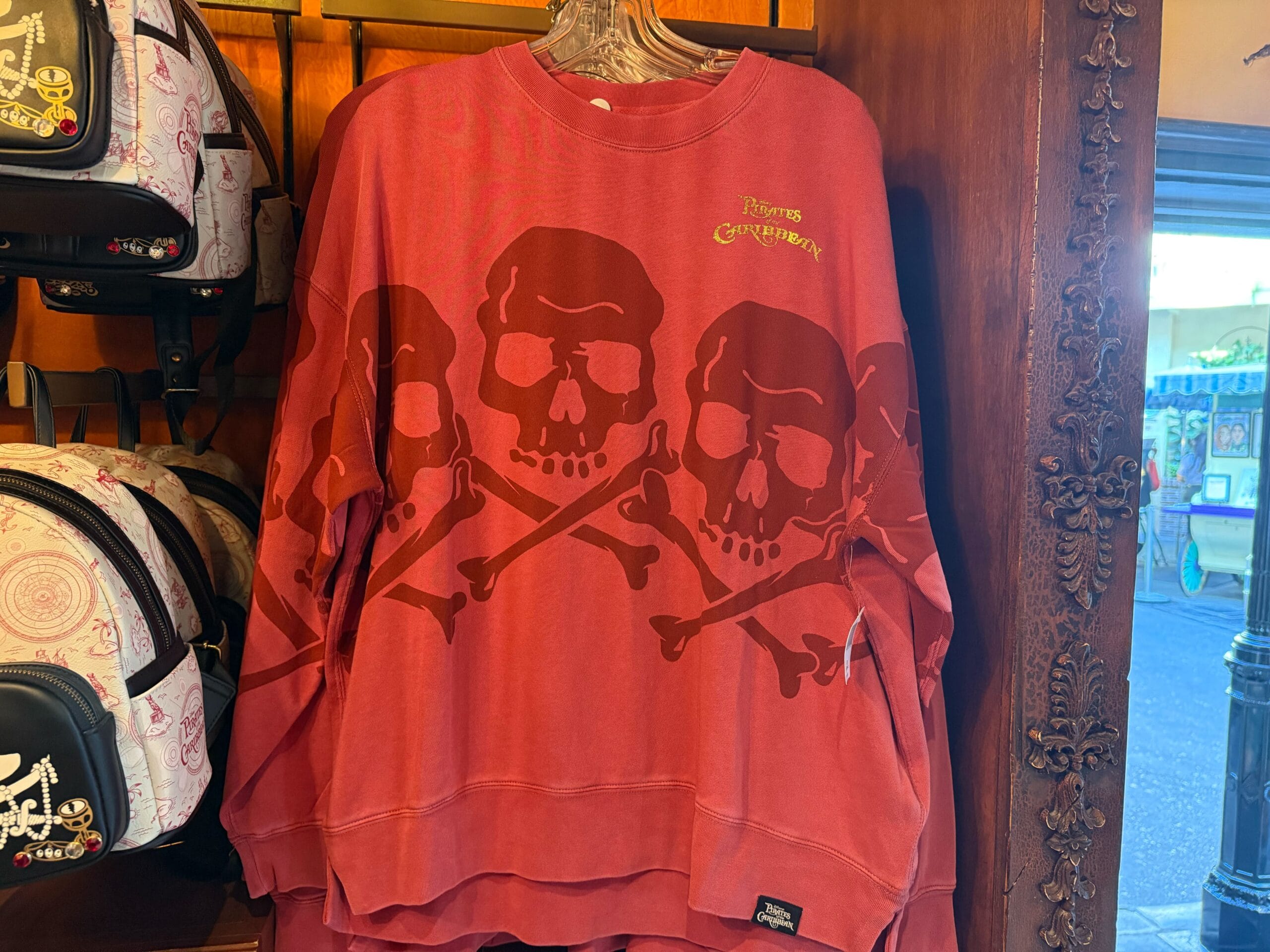 Red sweatshirt with bold skull and crossbones, perfect Pirates of the Caribbean apparel, hanging in a Disneyland store display.