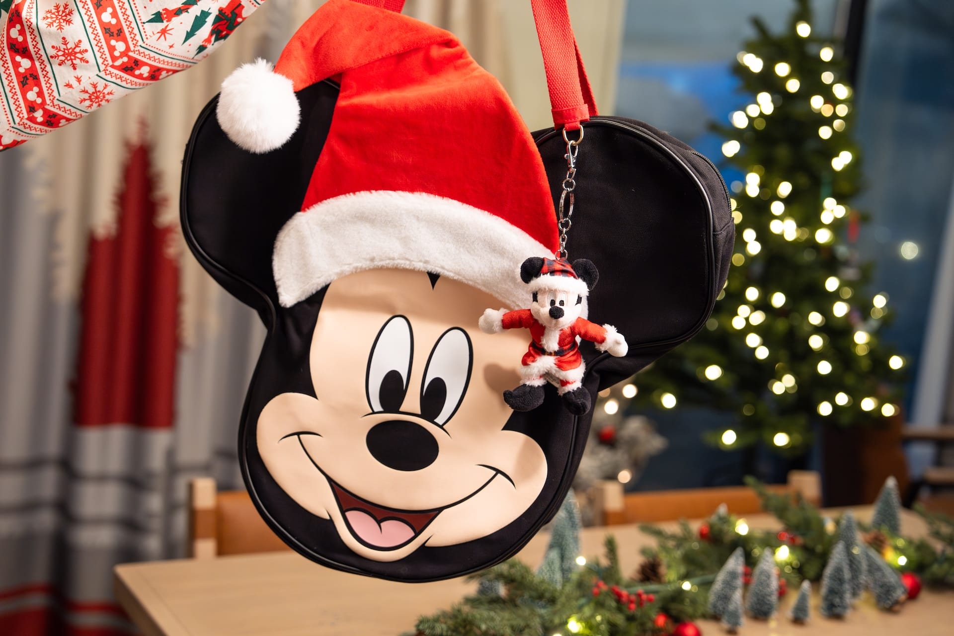 A Mickey Mouse purse with Santa hat and keychain; 2025 Holiday Merchandise at Disney Parks shines by the Christmas tree.