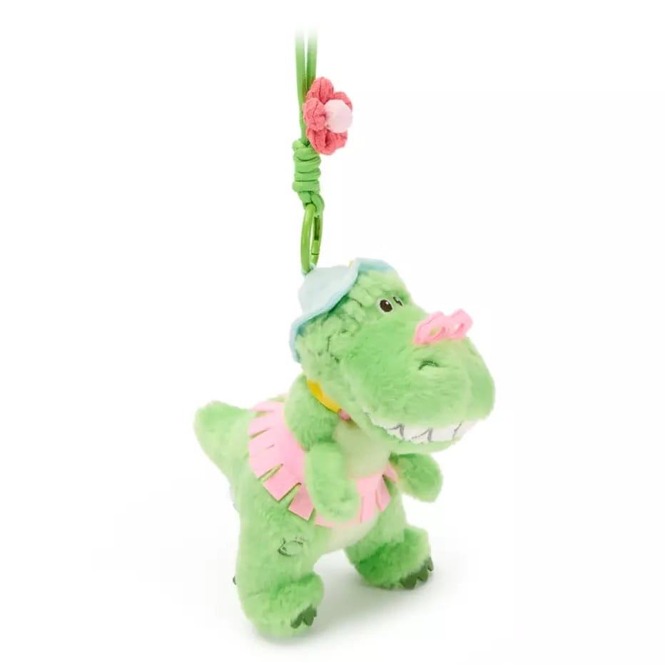 Plush green dinosaur keychain with pink skirt and blue hat, like Toy Story bag charms, now available in U.S.