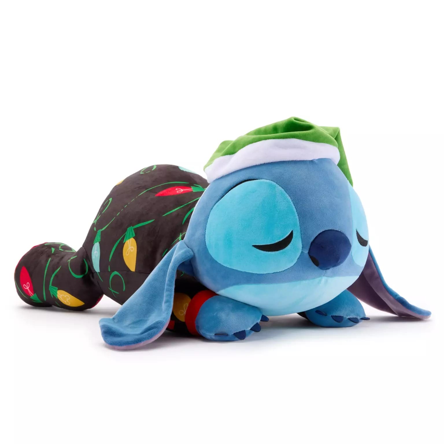 Plush Stitch toy in a green nightcap sleeps on a black blanket with holiday lights—Disney Christmas merchandise 2025.