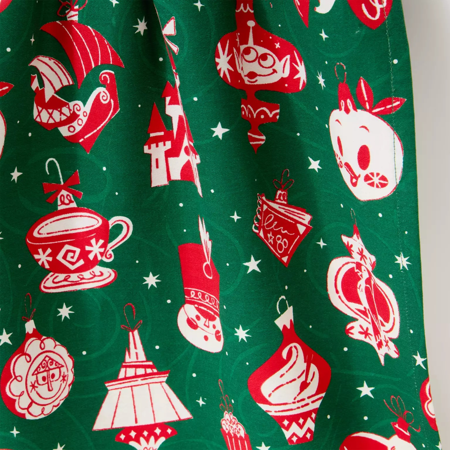 Green fabric with red and white Disney Store holiday ornaments, including a teacup, apple, and castle.