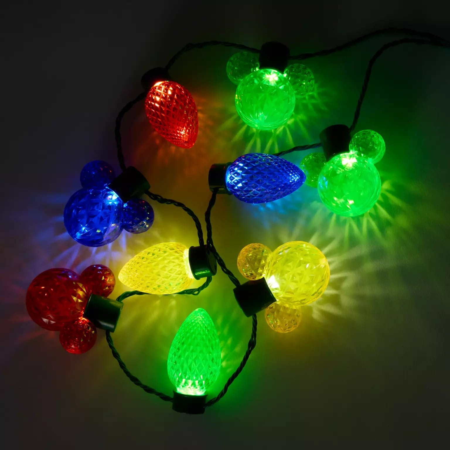 Disney Store's 2025 Christmas merchandise features bulb and mouse ear string lights in festive colors against a dark backdrop.