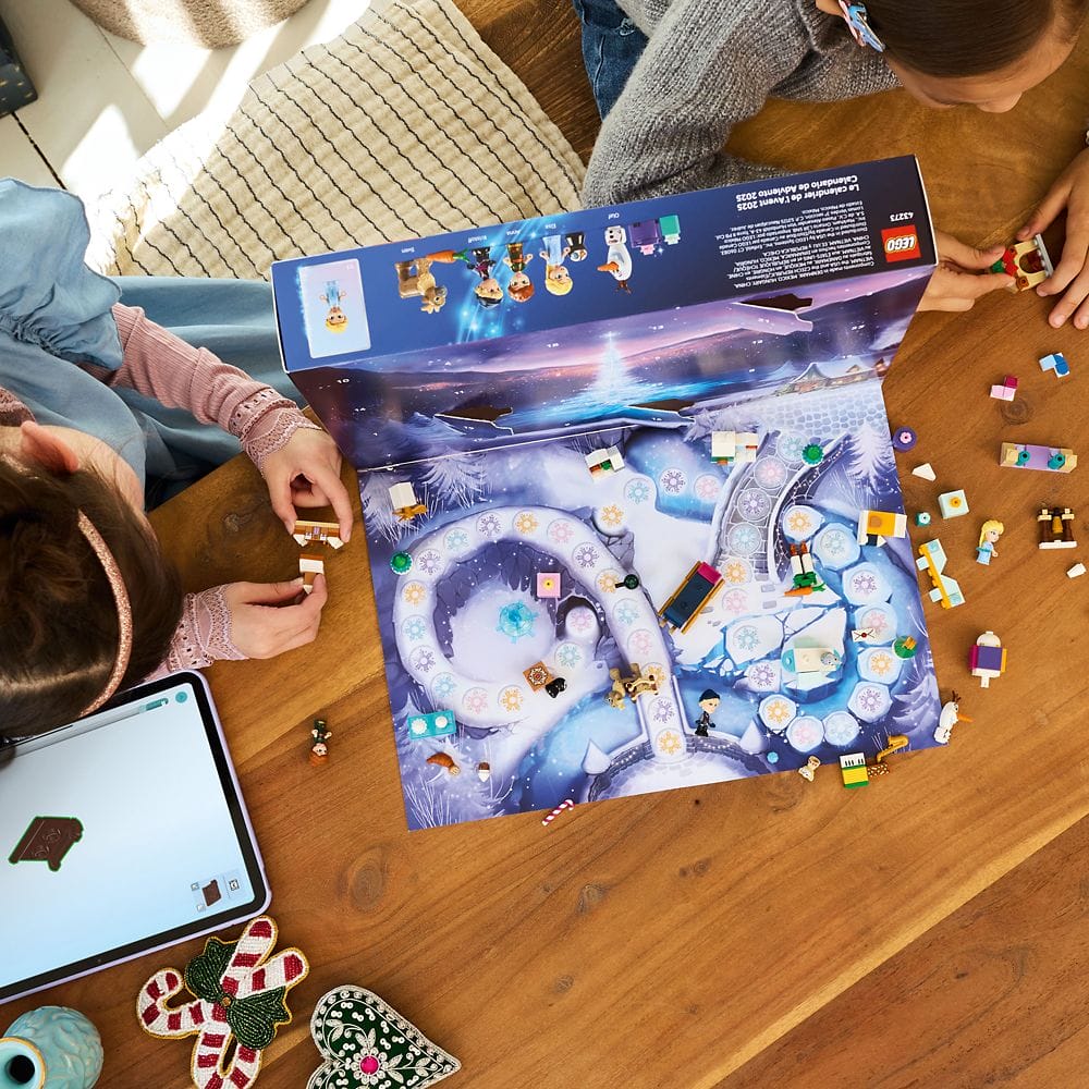Two children play a Frozen-themed board game with small figures and pieces on a wooden table.