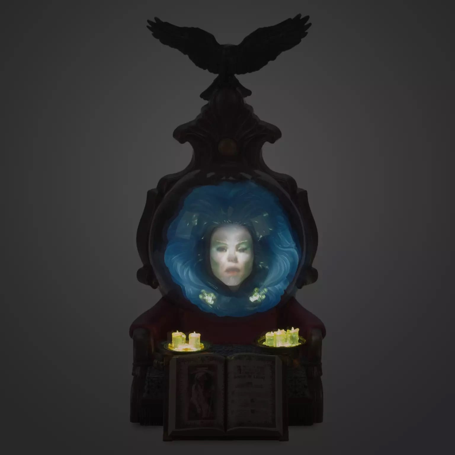 A mystical woman's face, like Madame Leota, appears in a glowing mirror above candles and an open book, framed by a raven.