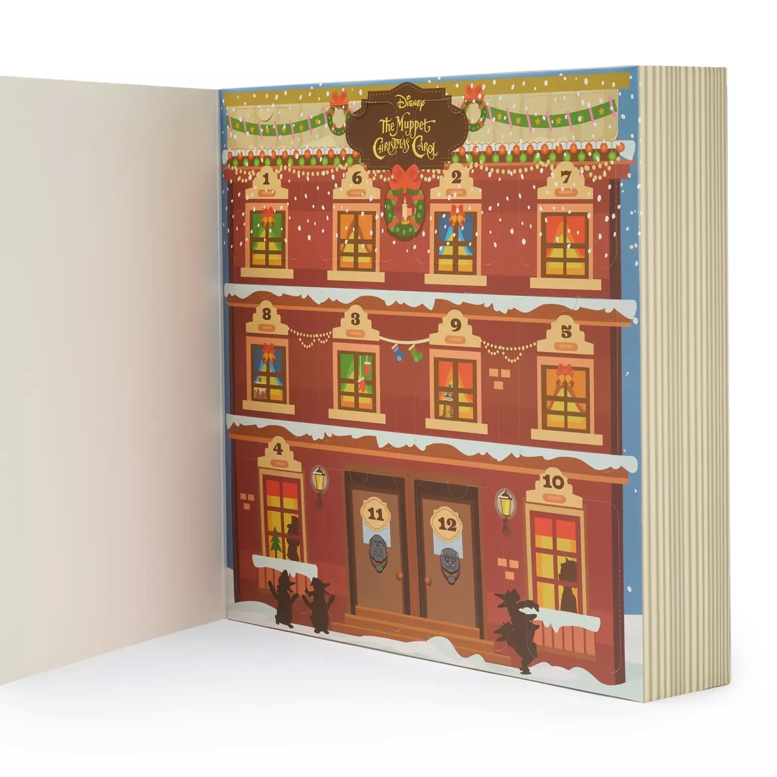An open book reveals a festive Christmas calendar building with numbered windows, garlands, and snowy countdown charm.