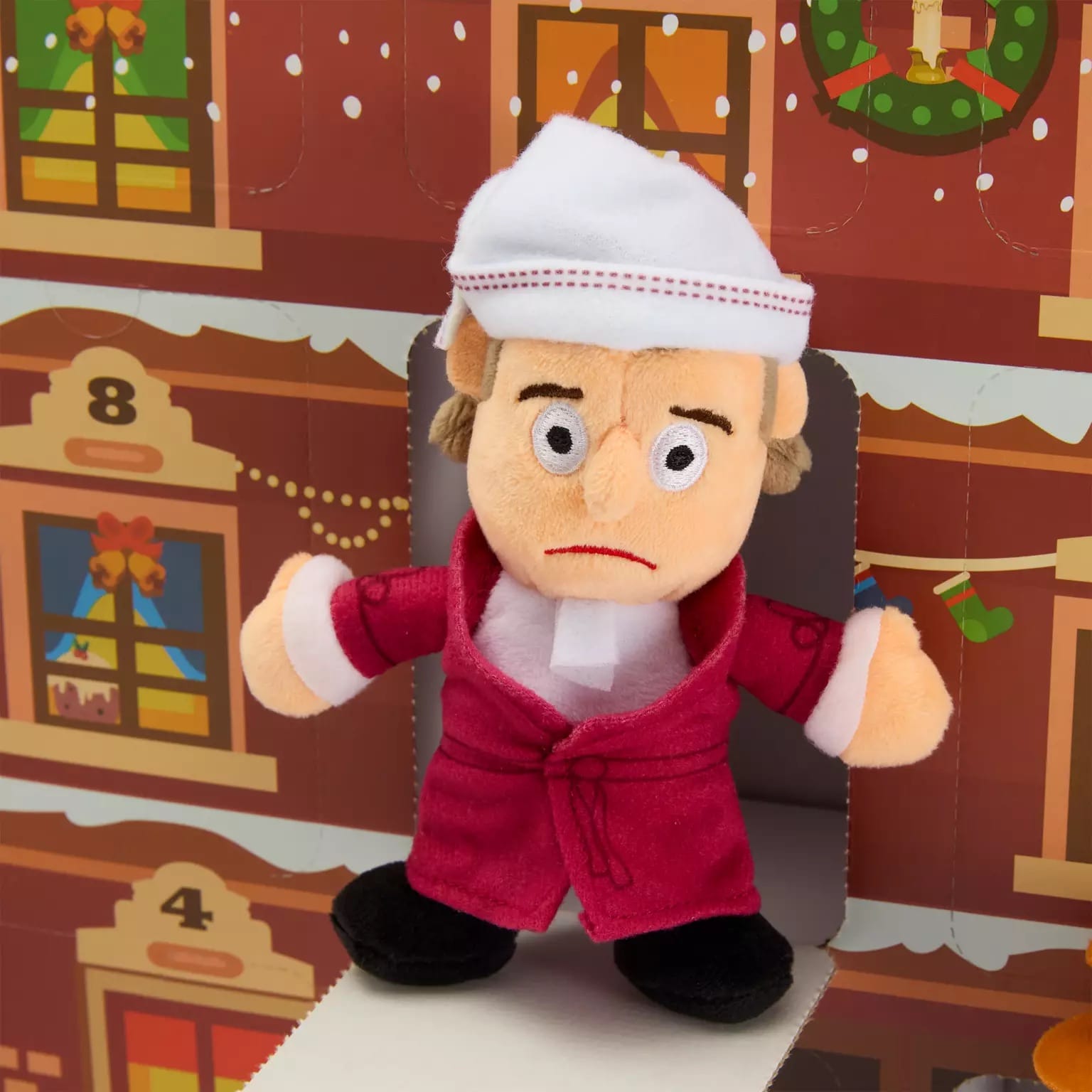 Plush doll of a man in red robe and white nightcap stands before a Christmas calendar with festive decorations.