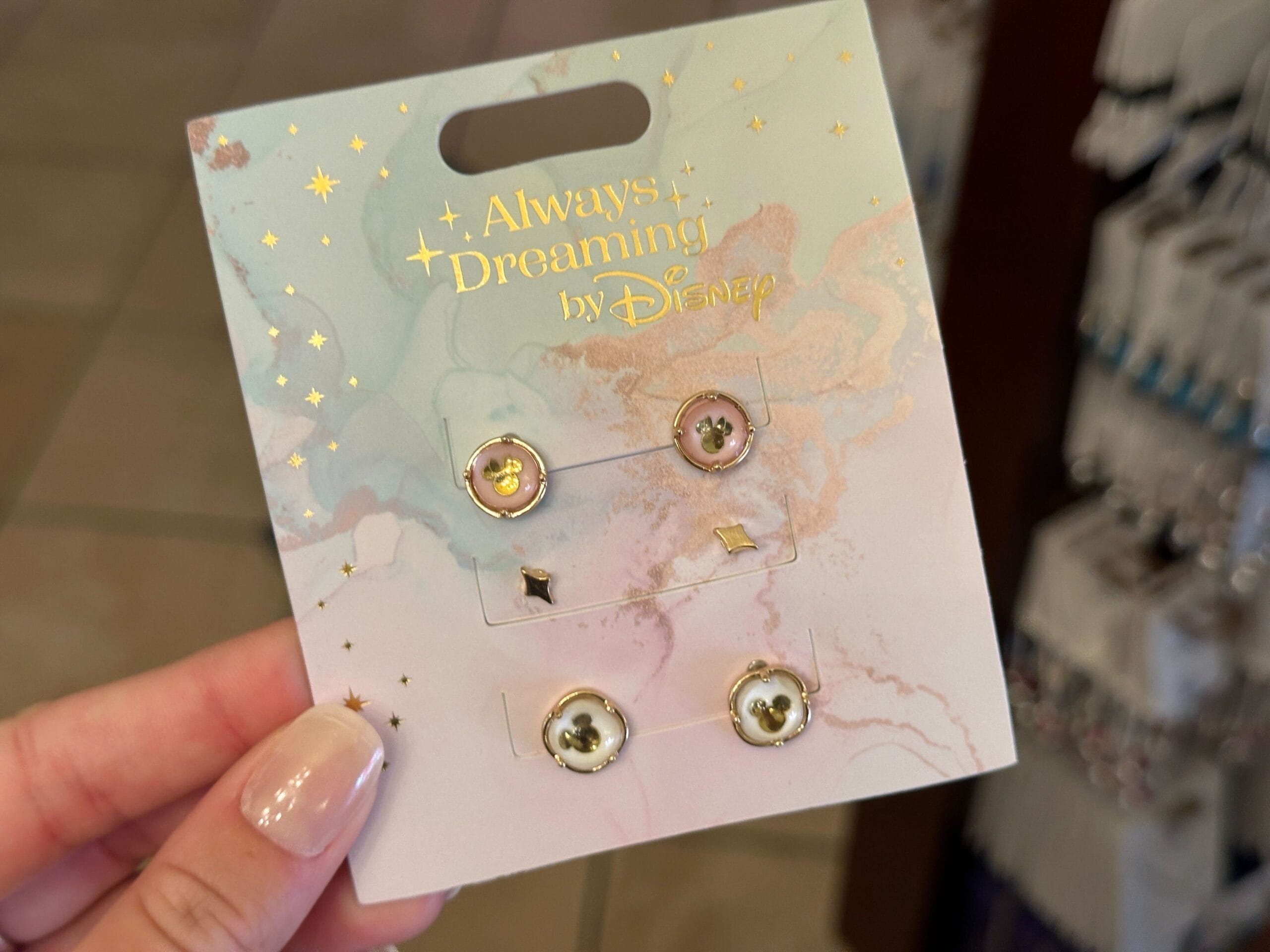 Hand holding a card with four pairs from the Disney jewelry collection, labeled "Always Dreaming by Disney.