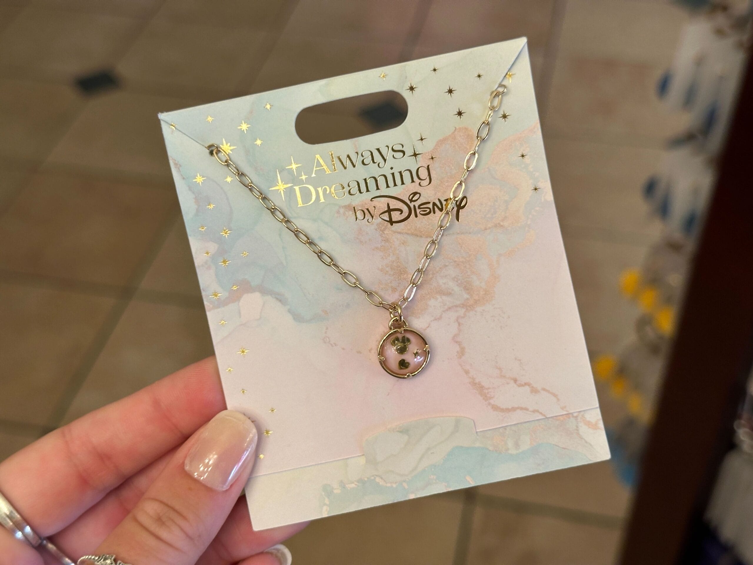 A hand holds a Disney necklace with a Mickey Mouse pendant, part of the magical Disney jewelry collection display.