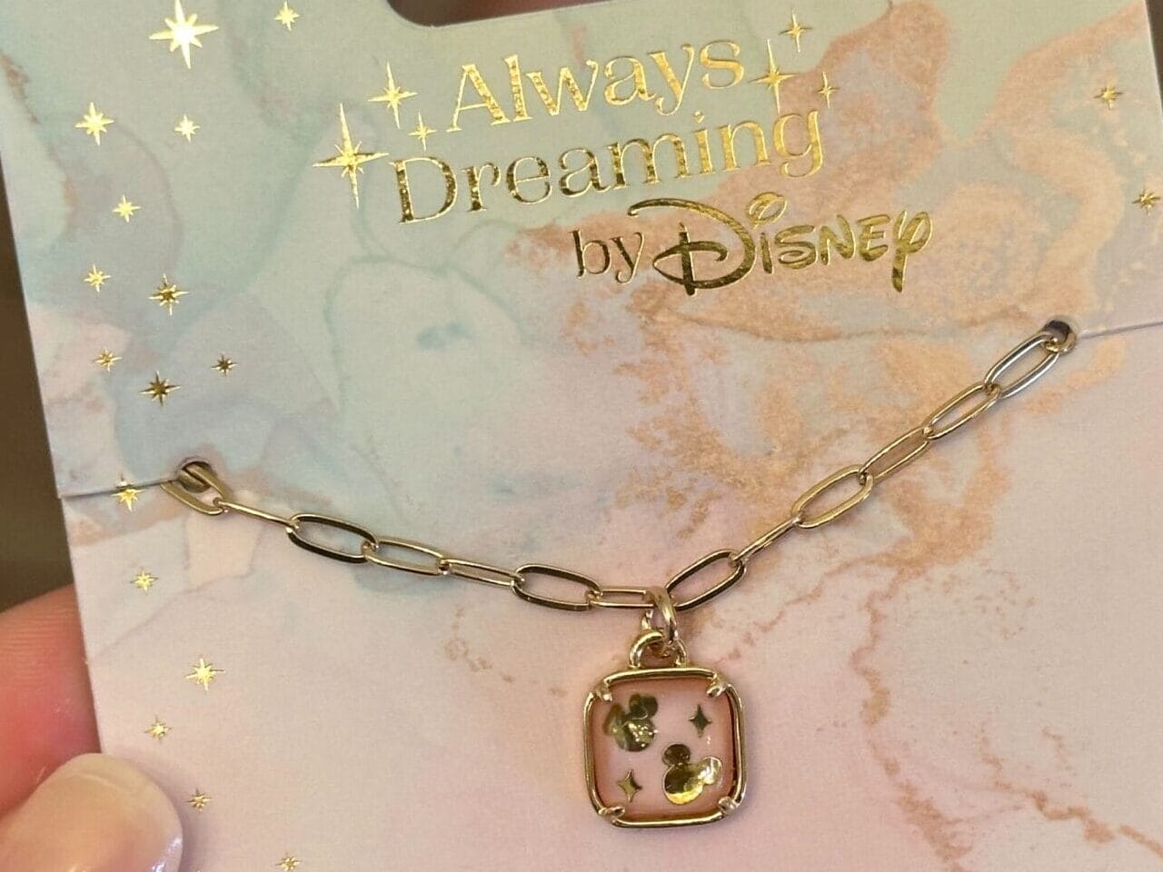 A hand holds a gold Disney bracelet with a Mickey Mouse charm from the Disney Jewelry Collection on a starry card.