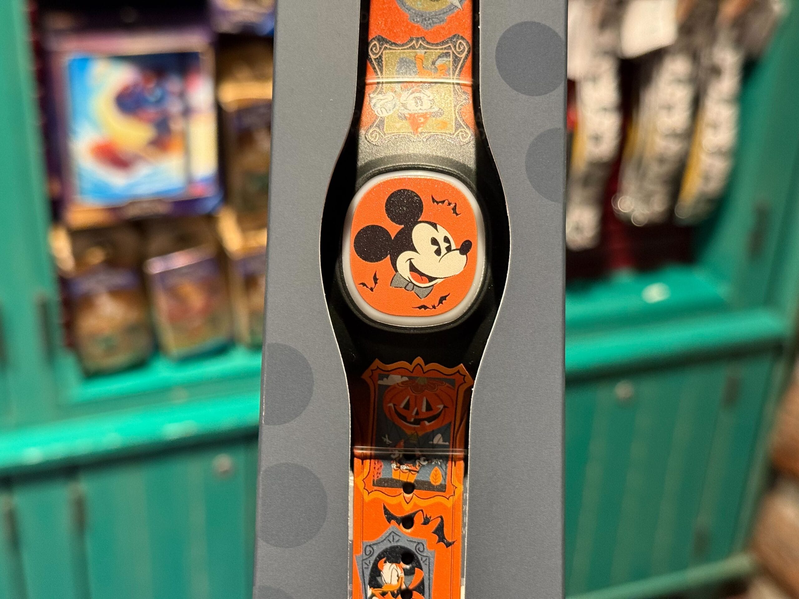 An orange Halloween MagicBand+ with a smiling Mickey Mouse in themed packaging, displayed in a Disneyland store.