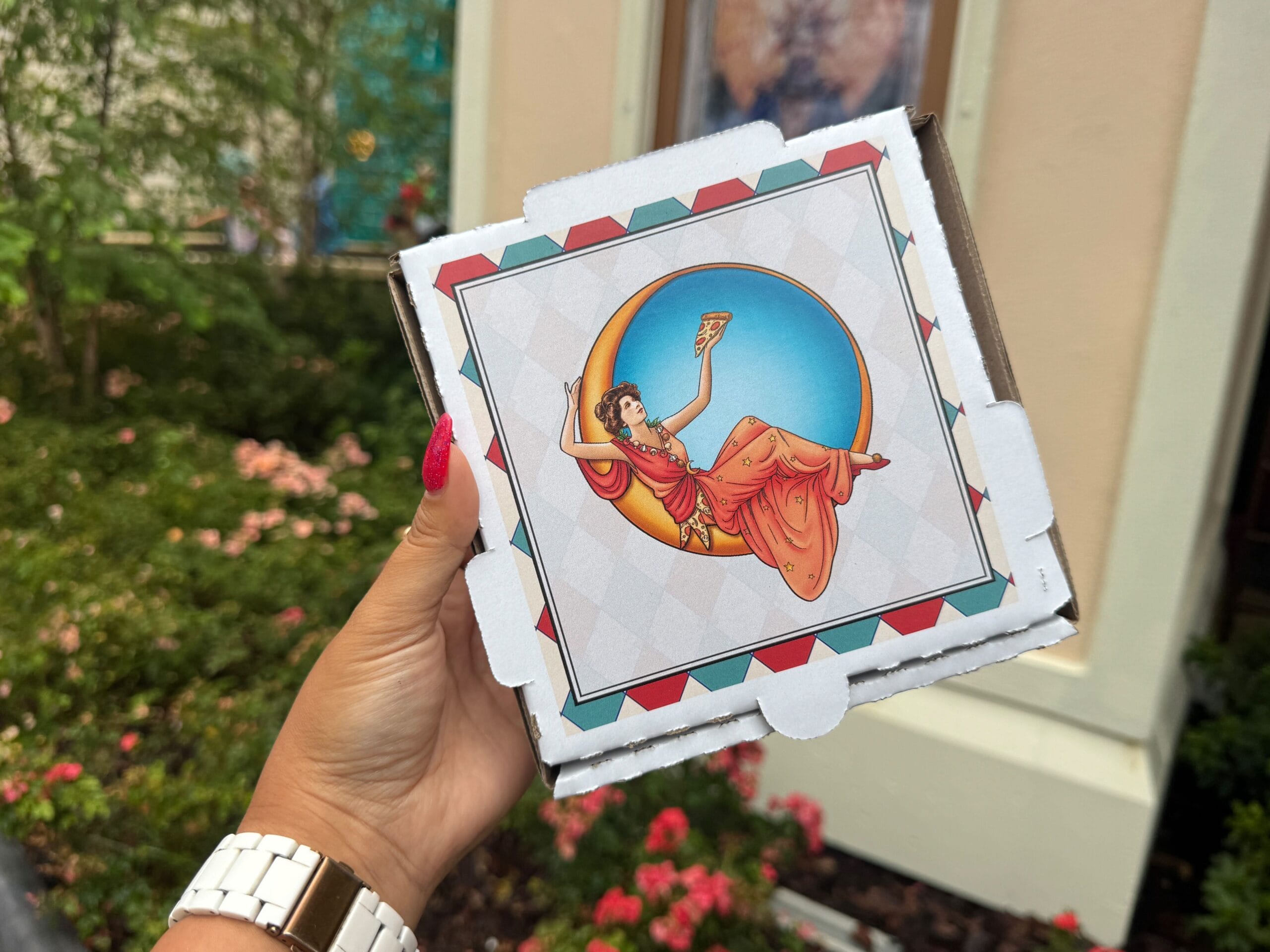 A hand holds a Brownie To-Go Box with art of a woman lounging in Pizza Moon style inside a crescent moon.