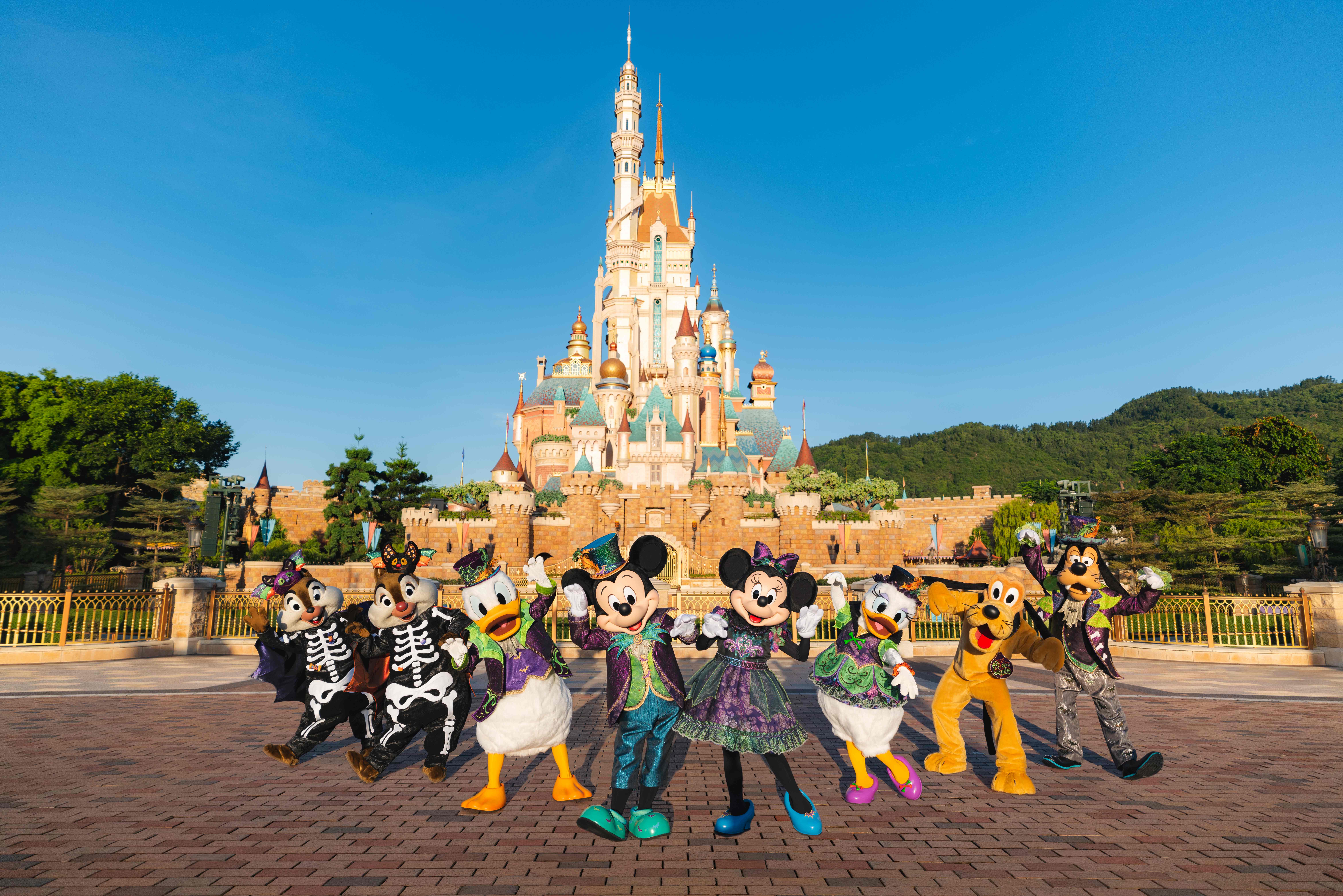 Disney characters and Disney Villains in Halloween costumes pose at Hong Kong Disneyland under a clear blue sky.
