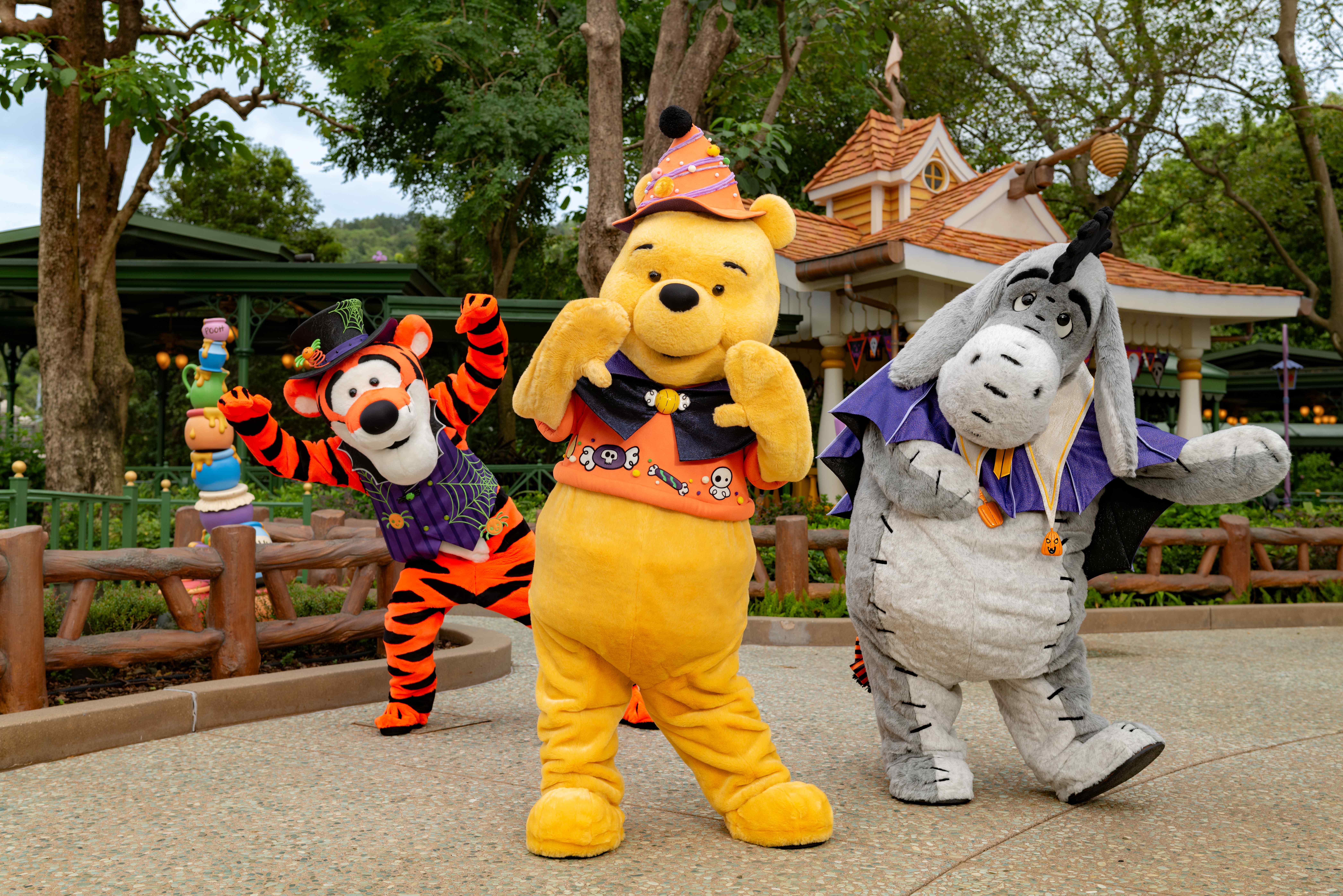 Winnie the Pooh, Tigger, and Eeyore in Halloween costumes pose outdoors at Hong Kong Disneyland.