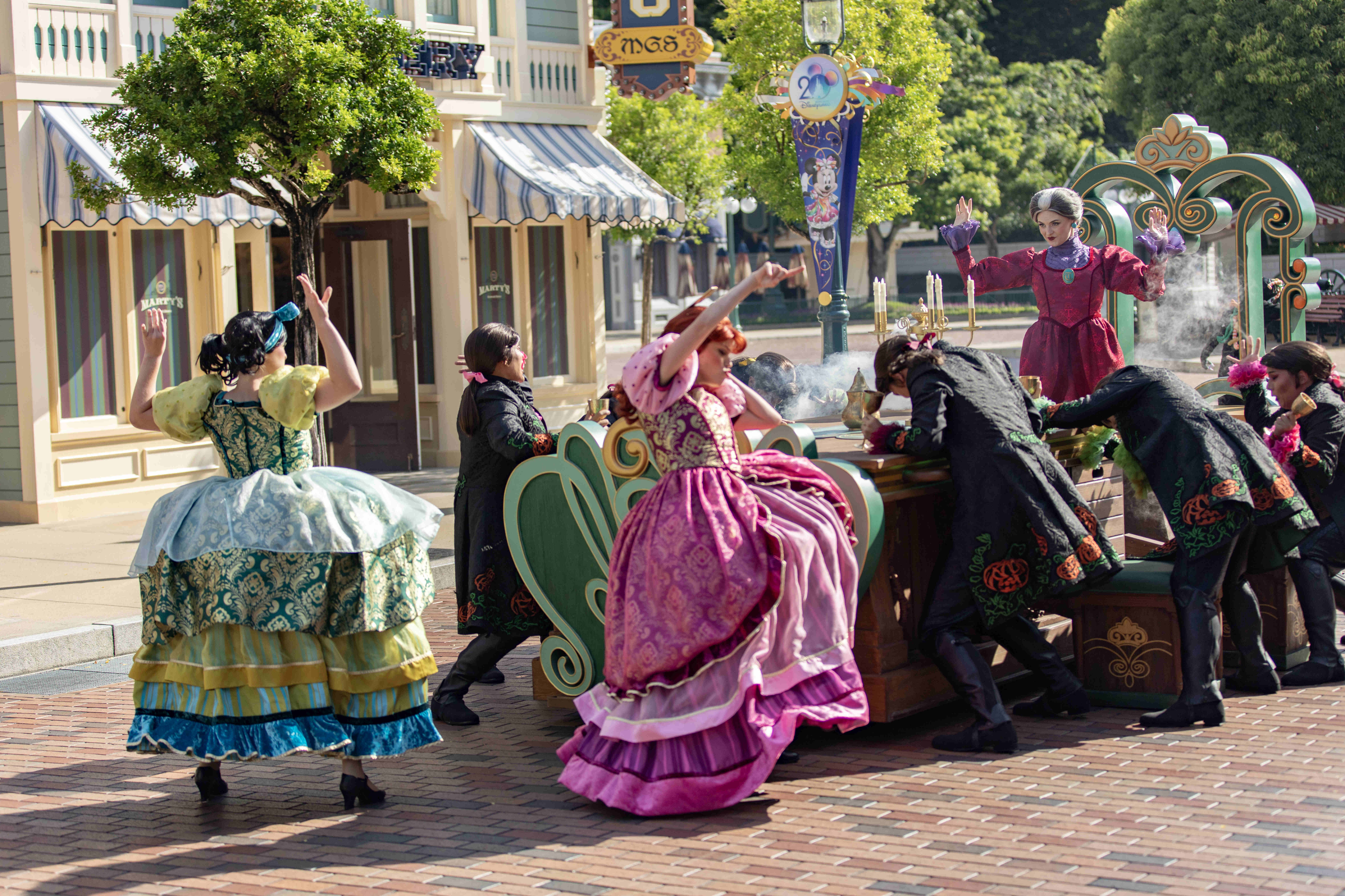 Performers in colorful, old-fashioned costumes dance and pose around a Halloween cart at Hong Kong Disneyland.